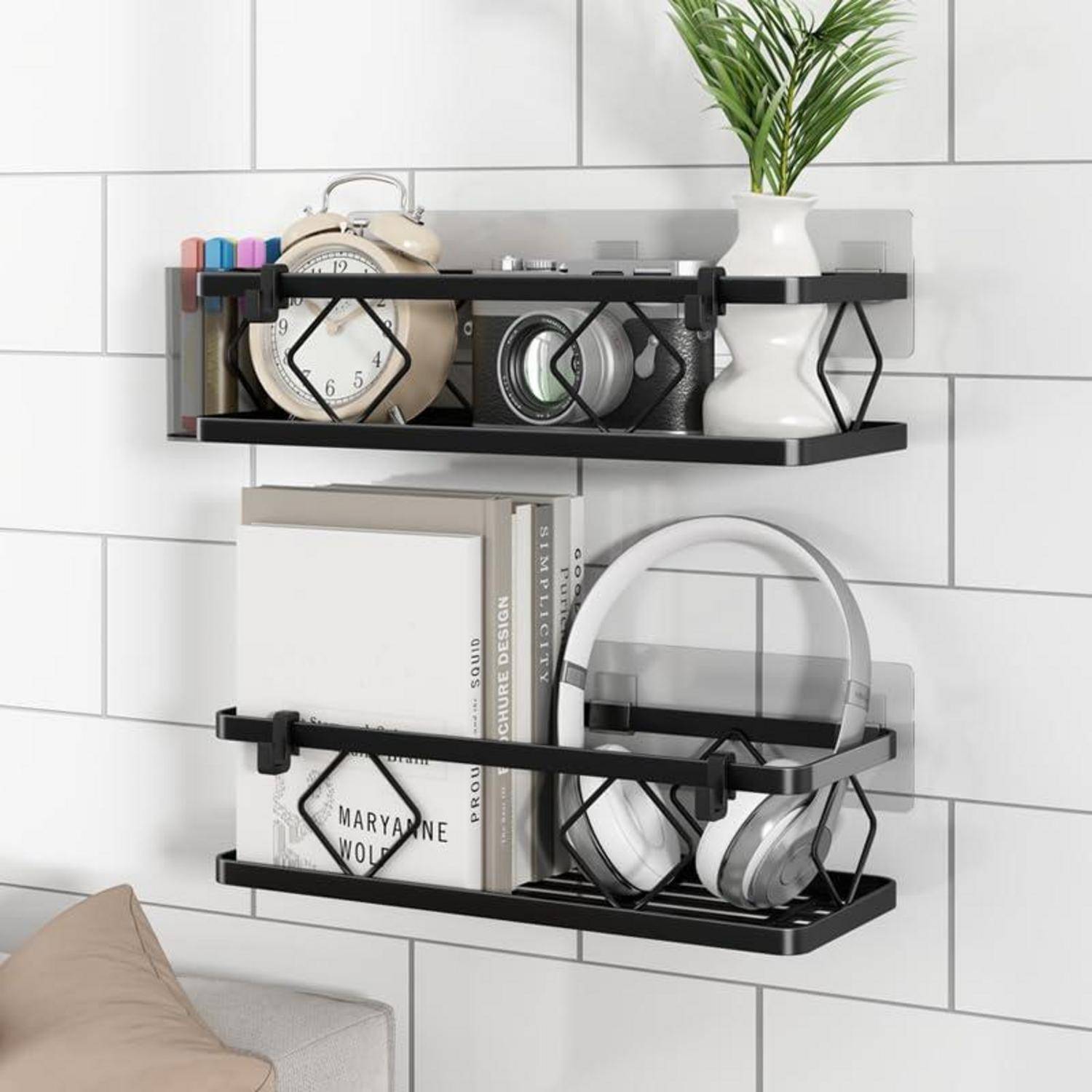 An der Wand montierte schwarze Regale, auf denen ein Wecker, Bücher, Kopfhörer, eine Vase mit Grünpflanzen und ein kleiner Organizer an einer weißen Fliesenwand angebracht sind.