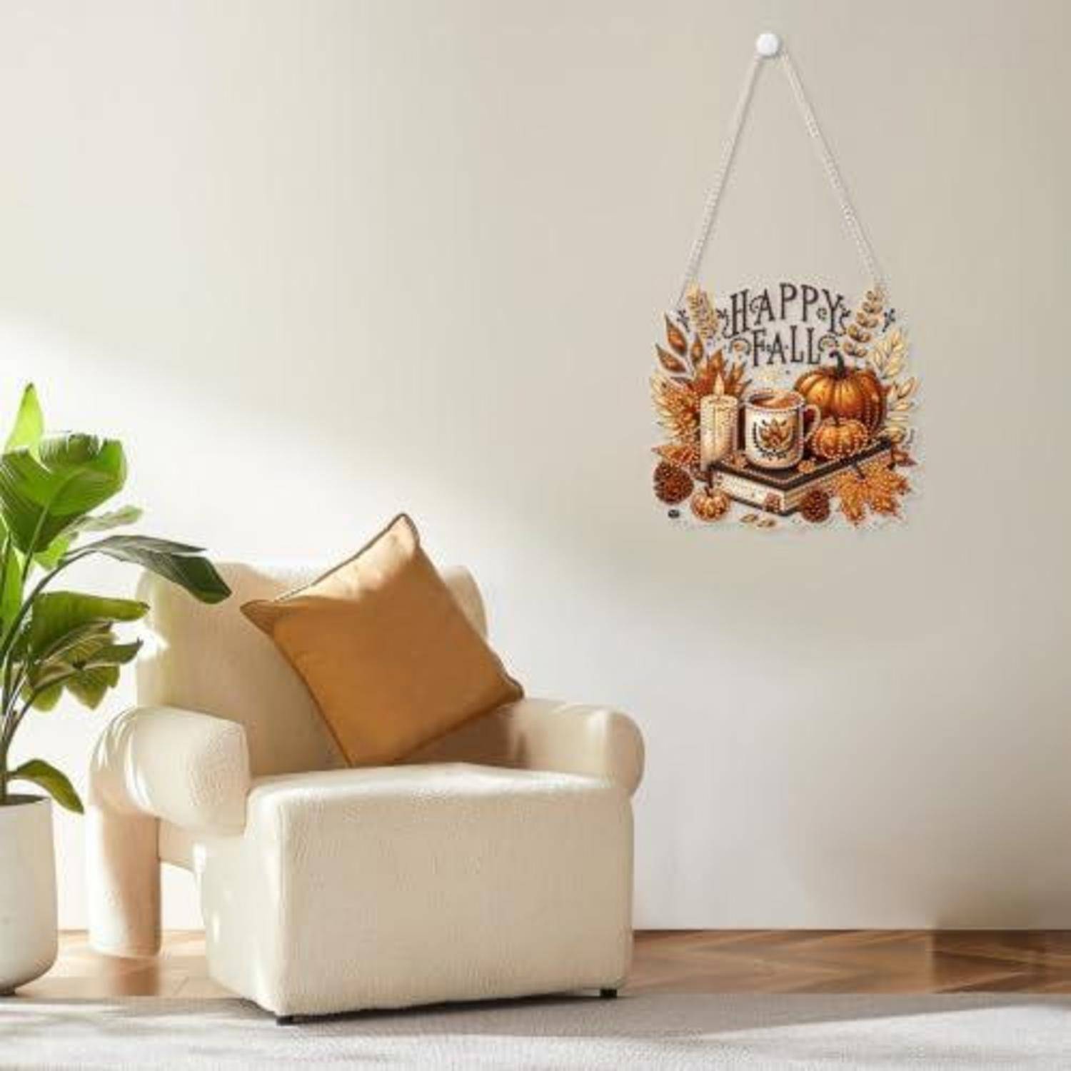 Gemütliches Wohnzimmer mit cremefarbenem Sessel und Pflanze; Wandbehang liest „Happy Fall" mit Kürbissen und Herbstblättern.