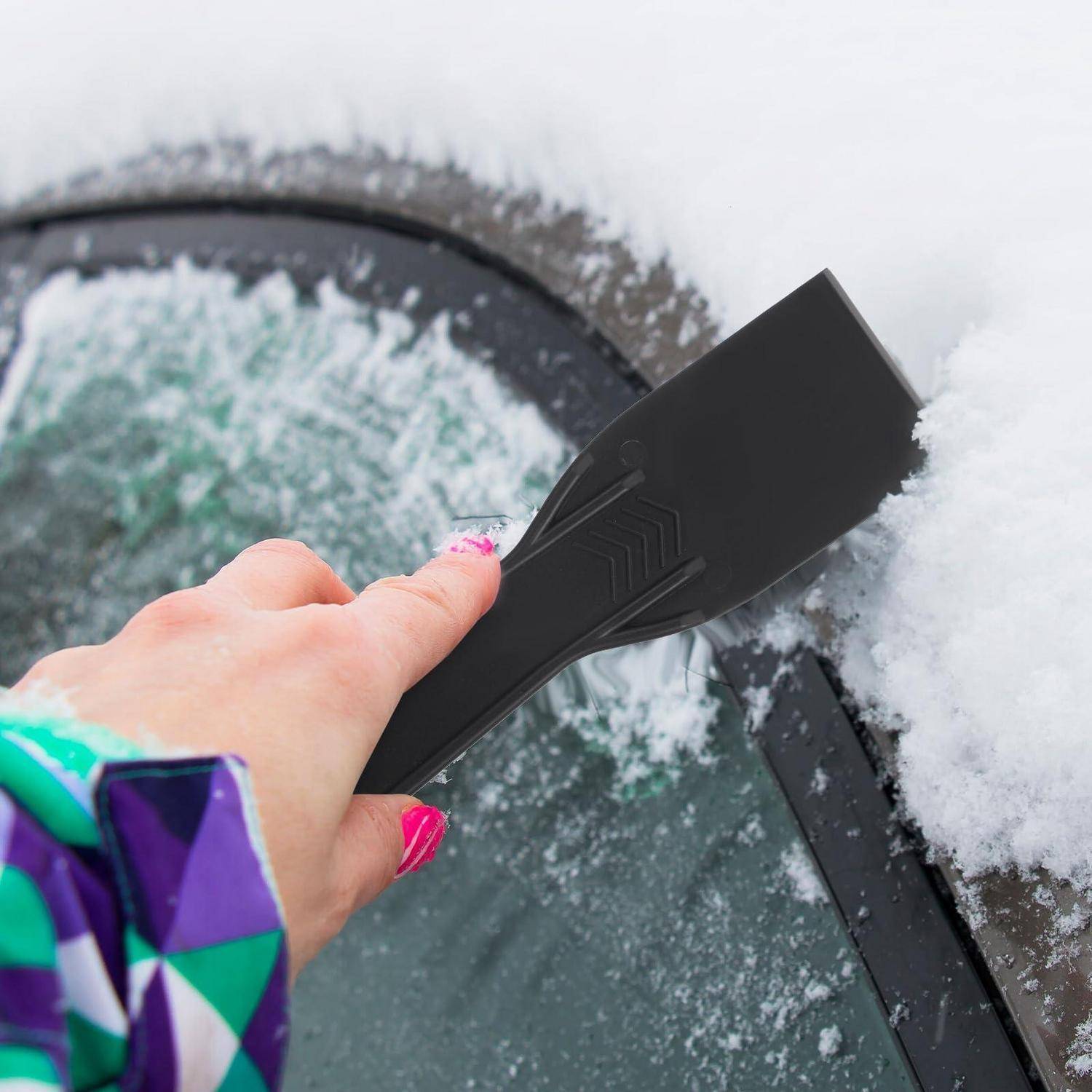 Eine Hand mit einem schwarzen Eiskratzer, um Schnee von einer Autowindschutzscheibe zu entfernen.