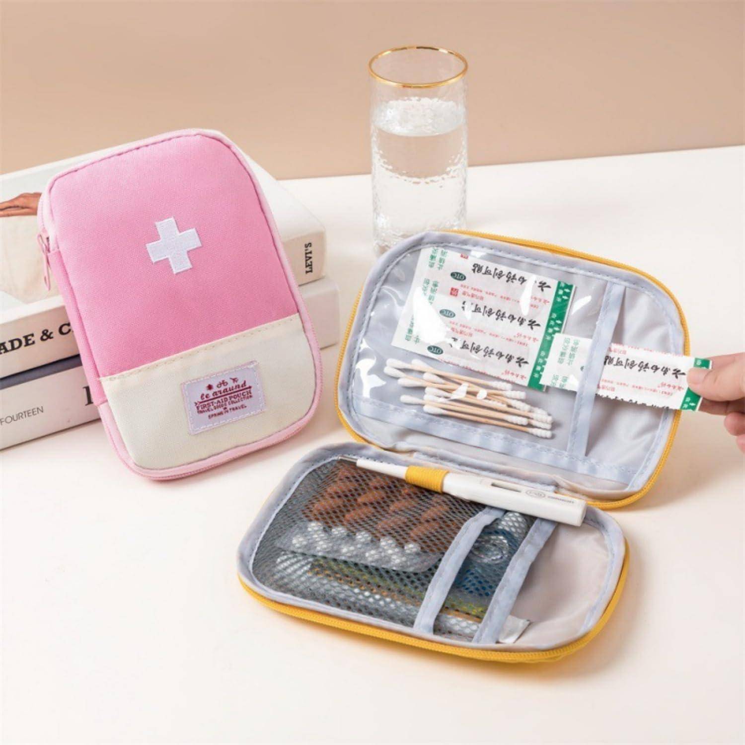 Zwei kleine Erste-Hilfe-Taschen, eine rosa und eine offene graue, mit Medikamentenpäckchen, Wattestäbchen und Vorräten auf einem Tisch neben einem Glas Wasser.