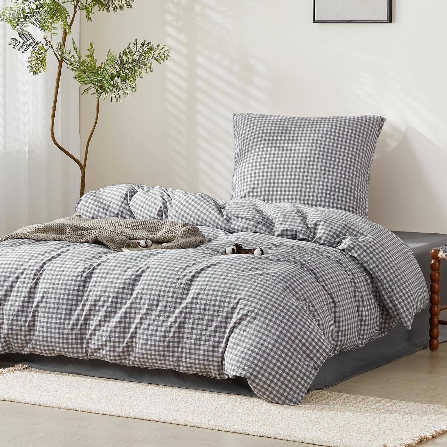 Graues Gingham-Bettwäsche auf einem niedrigen Bett mit Kissen und Decke in einem hellen, minimalistischen Schlafzimmer mit einer Topfpflanze.