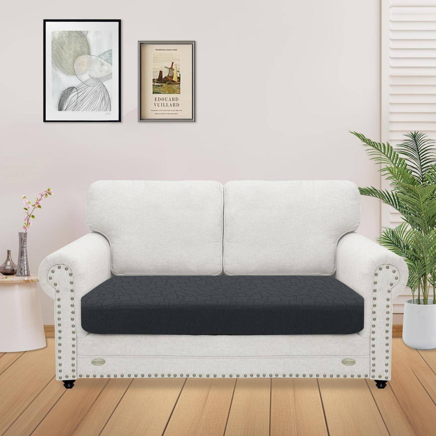 Weiße zweisitzige Couch mit schwarzem Kissen in einem hellen Wohnzimmer, mit gerahmten Wandbildern, Pflanzen und hellem Holzfußboden.