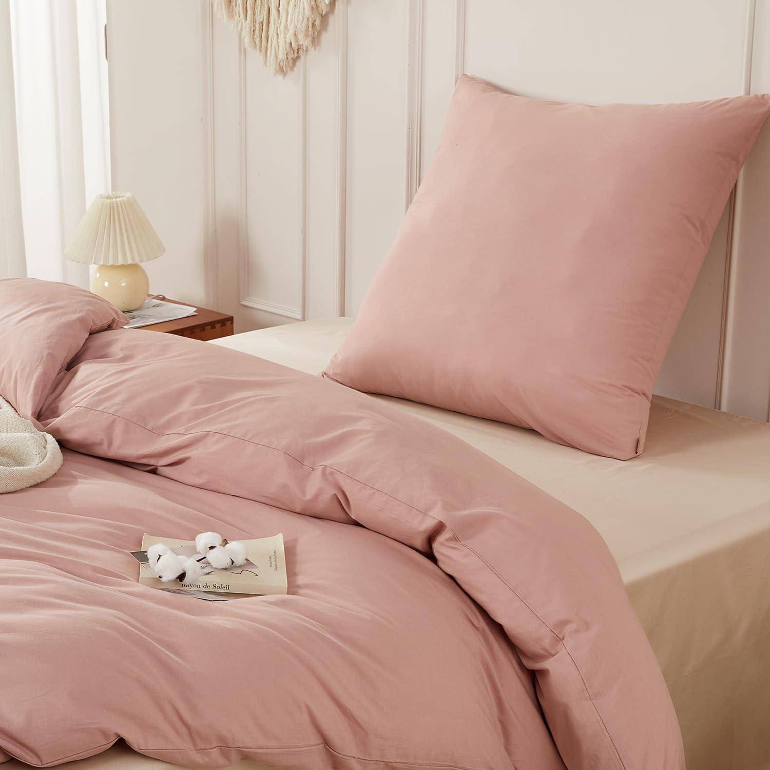 Rosa Bettwäsche mit einem großen Kissen und einer Bettdecke auf einem ordentlich gemachten Bett in einem sanften, neutralen Schlafzimmer.