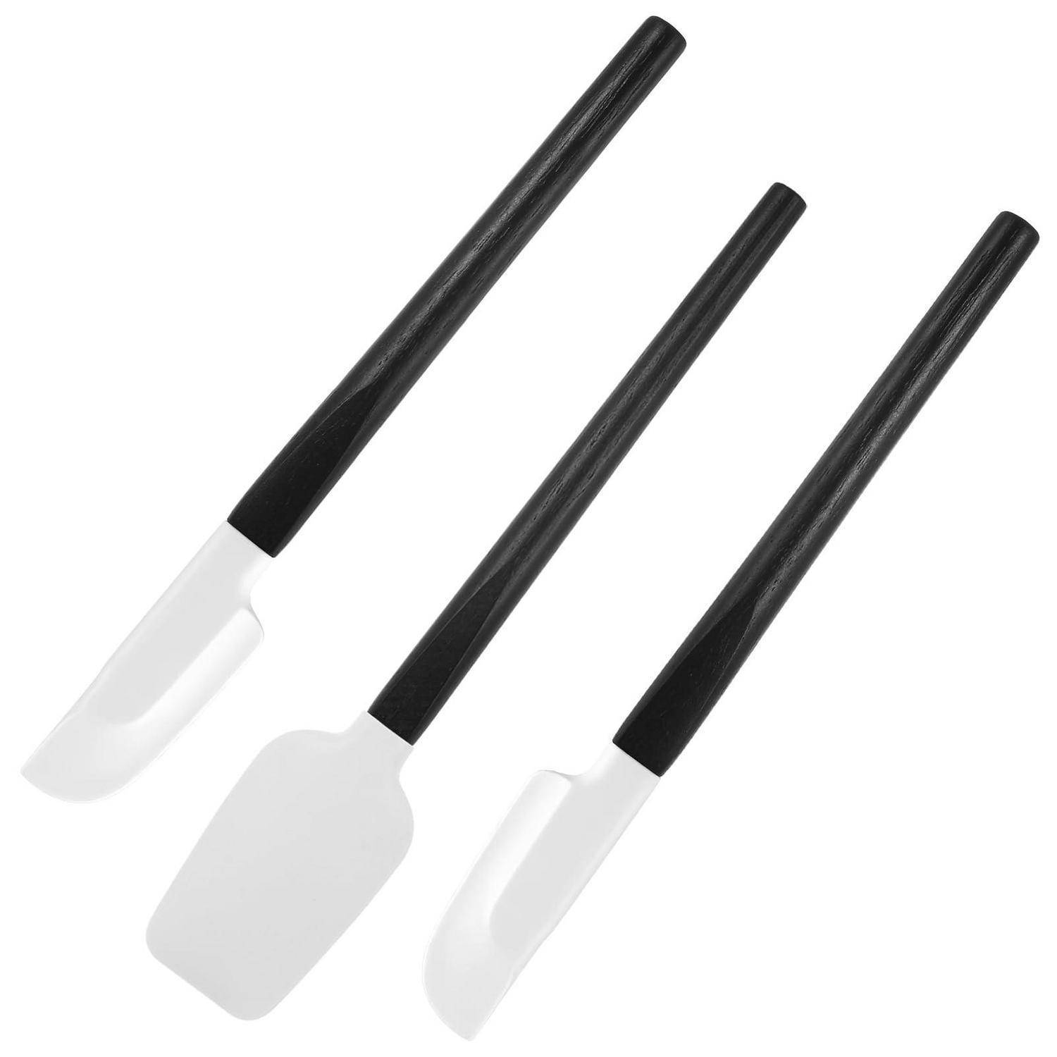 Drei Küchenspachtel mit schwarzen Griffen und weißen Silikonköpfen, diagonal auf weißem Hintergrund angeordnet.