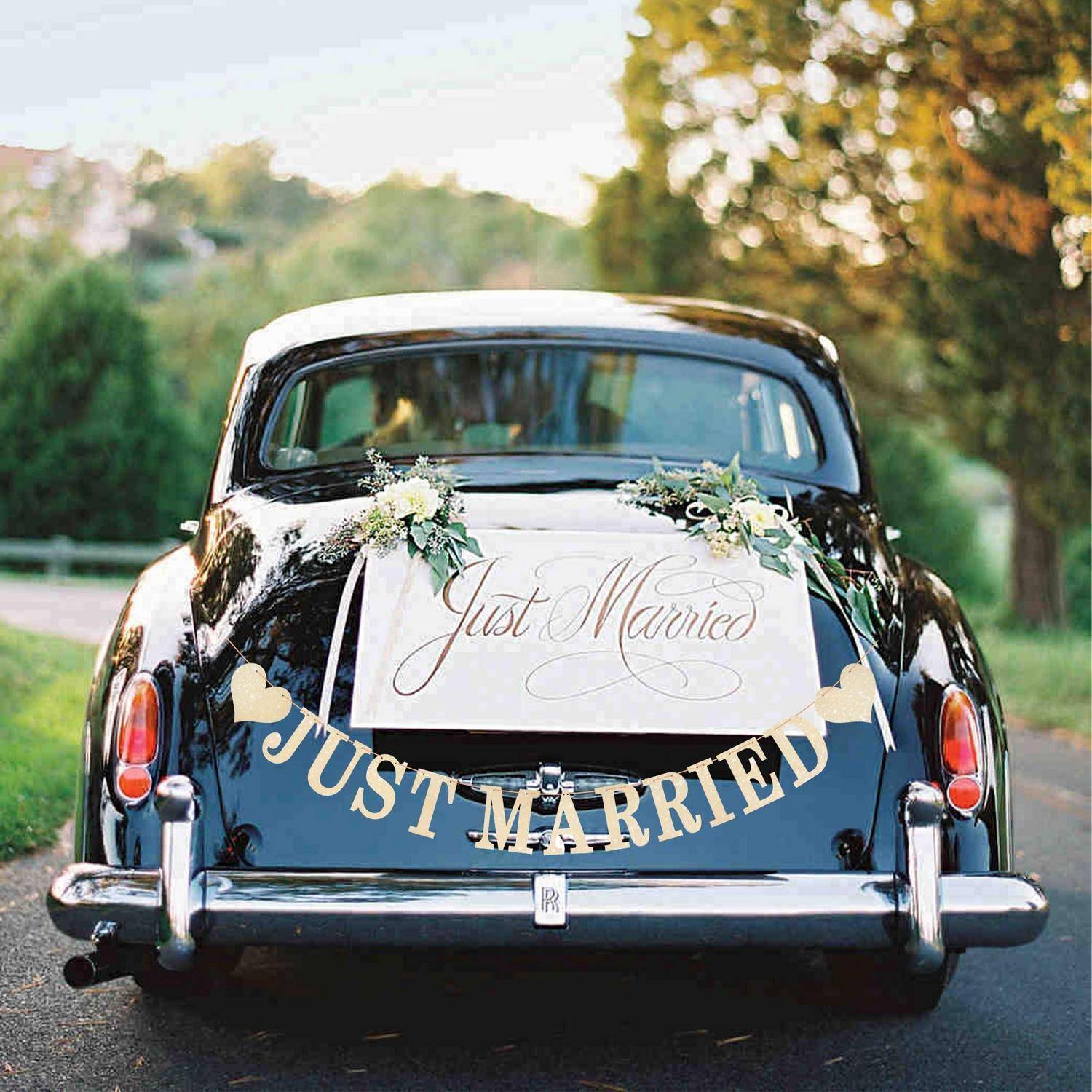 Rückansicht eines vintage schwarzen Autos, das für eine Hochzeit dekoriert ist, mit "Just Married""-Schildern und Blumenarrangements auf der Rückseite.
