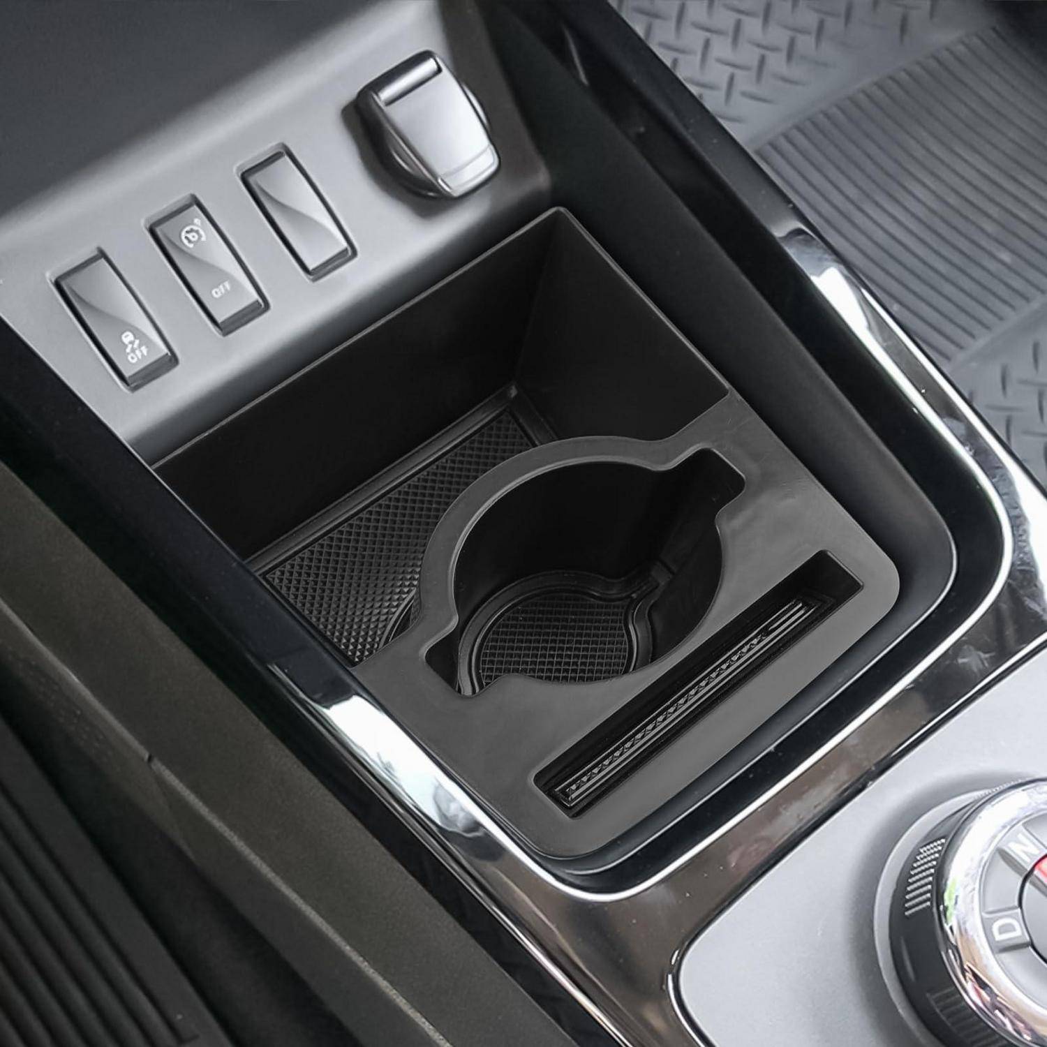Mittelkonsole des Autos mit Getränkehalter, Ablage und Schalterknöpfen für die Gangwahl neben den Armaturenbrettreglern.