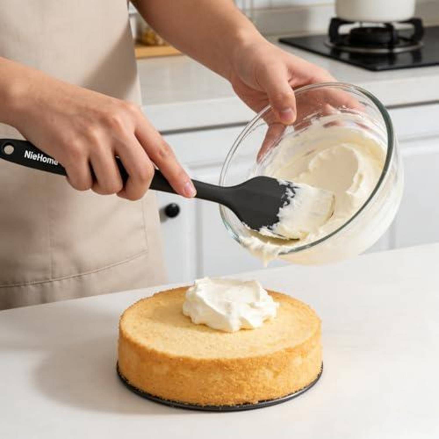 Eine Person verteilt Glasur mit einem Spatel auf einen Schwammkuchen in einer Küche.