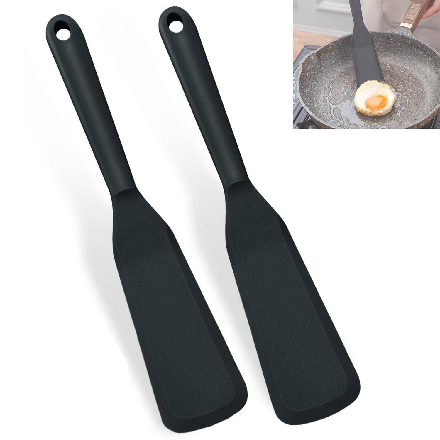 Zwei schwarze Silikonspatel mit Aufhängelöchern, daneben eine Vergrößerung eines Spatels, der ein Ei in einer Pfanne wendet.