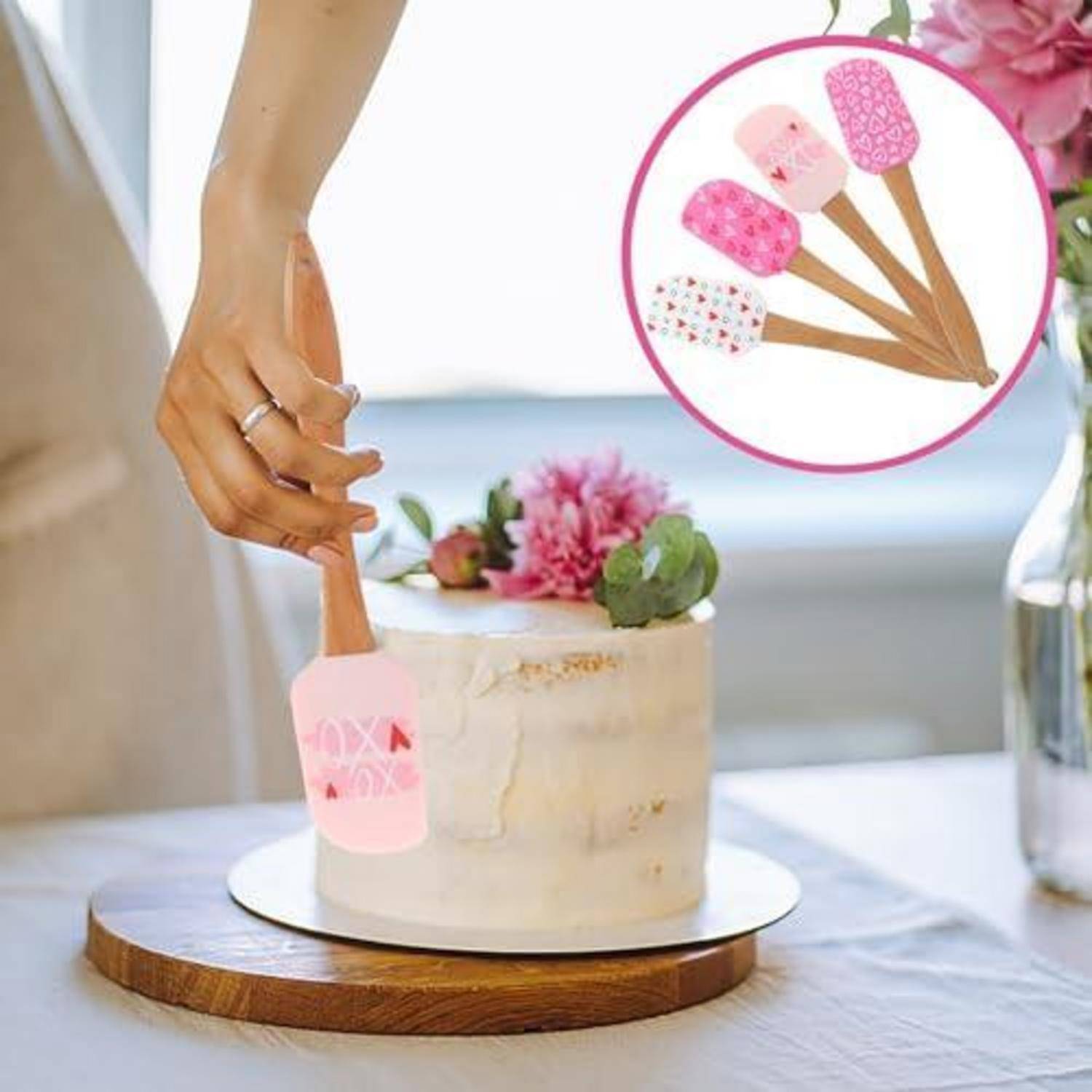 Eine Hand platziert einen rosa gemusterten Teigschaber auf einem glasierten Kuchen, mit einer kleinen Einfügung, die vier passende Teigschaber-Designs zeigt.