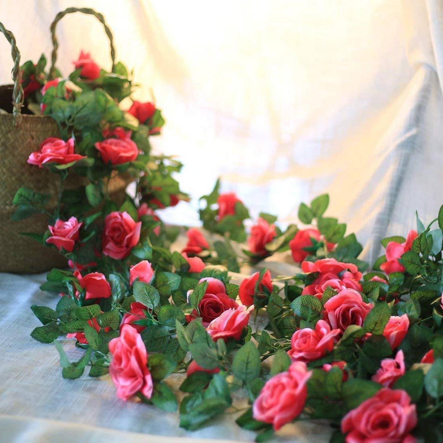 Ein Korb, der über mit roten und rosa Rosengirlanden überläuft, die auf einer weiß drapierten Oberfläche angeordnet sind.