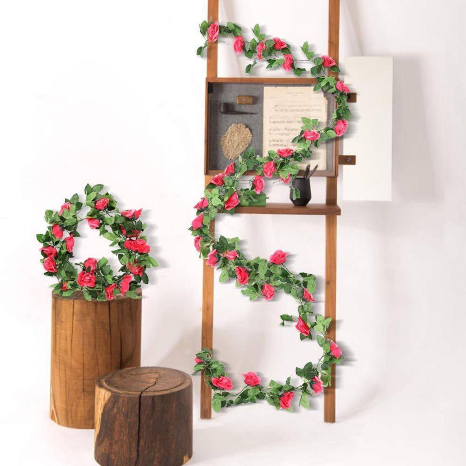Dekorative rosa Rosen- und grüne Blattgirlanden, die um ein Holzleitungsregal und einen kleinen Baumstumpf gewickelt sind, mit einem passenden Blumenkranz auf einem Holzpodest.