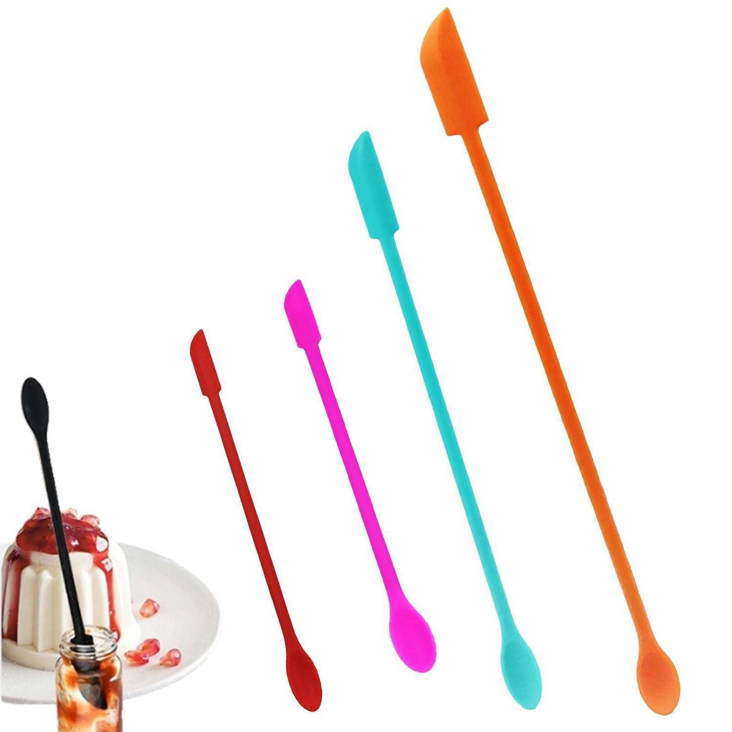 Fünf farbenfrohe Löffel mit langen Stielen und flachen Spatseln stehen neben einem Dessertwecker und einem Teller Pudding mit Granatapfelkernen.