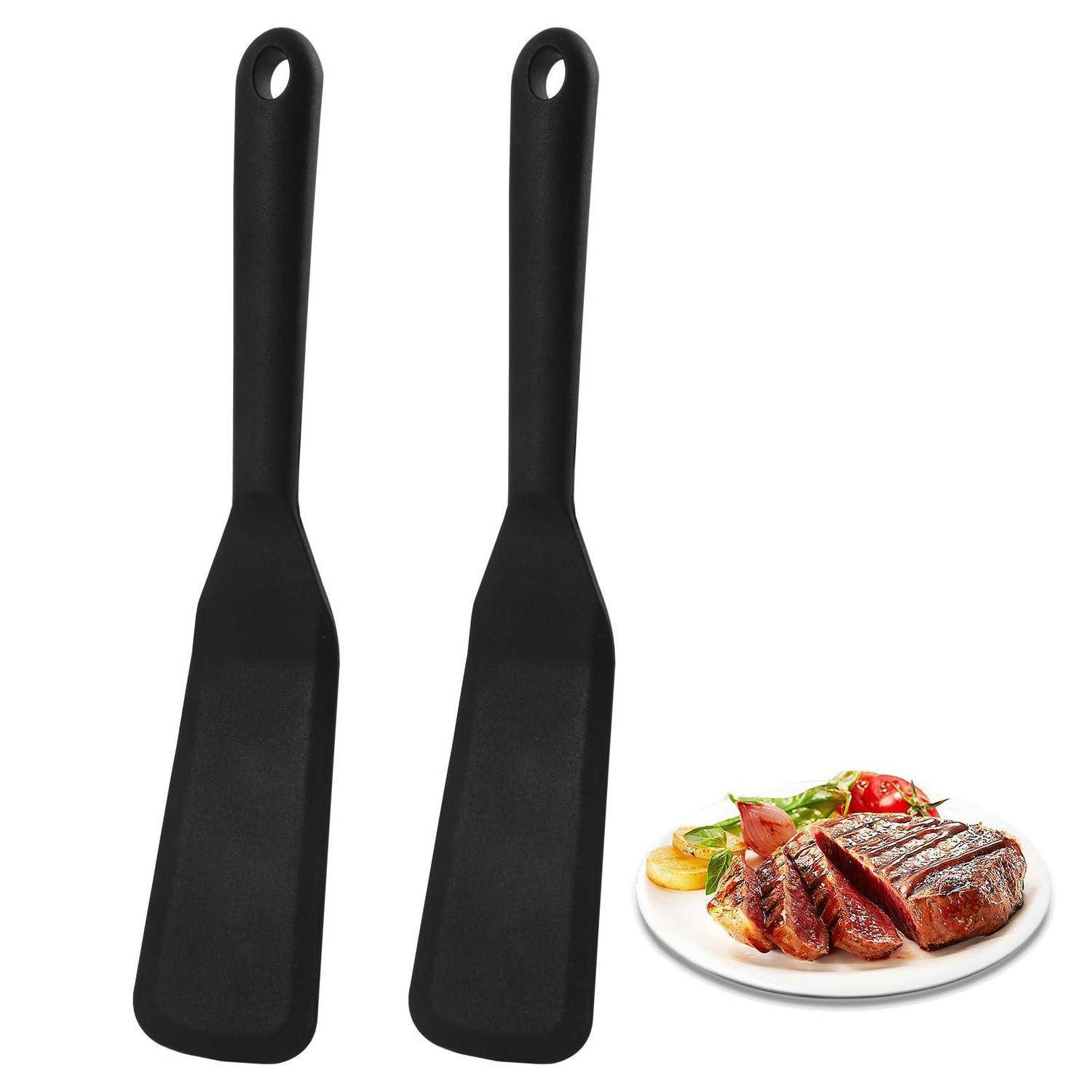 Zwei schwarze Spachteln neben einem angerichteten Steakdinner, was auf Kochgeschirr zum Servieren oder Wenden von Speisen hindeutet.