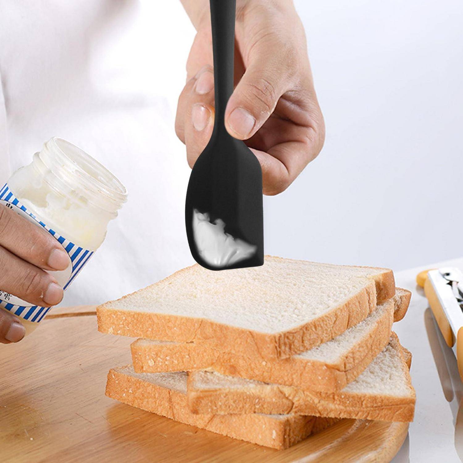 Eine Person verteilt weiße Creme auf gestapelten Brotscheiben mit einem schwarzen Spatel.