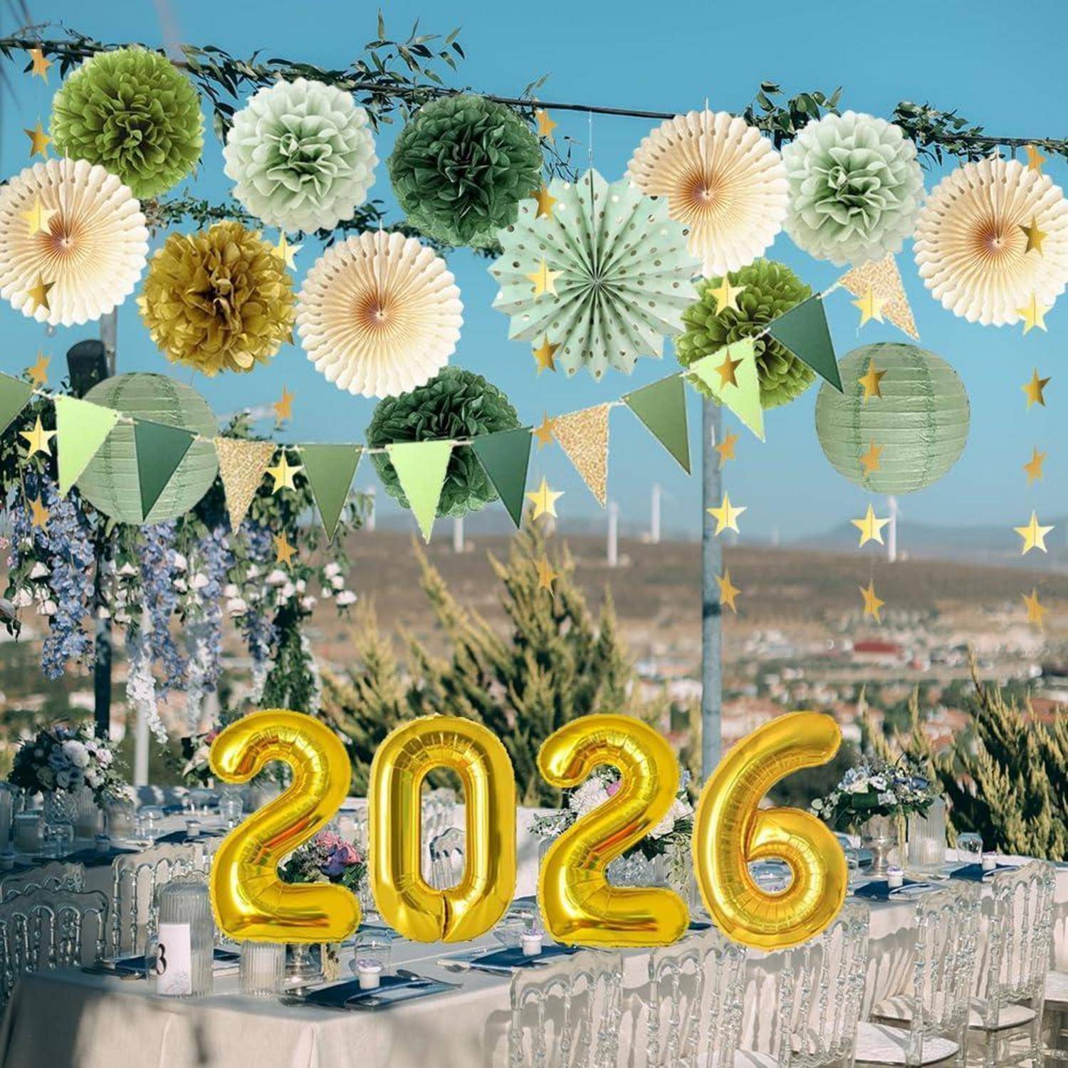 Outdoor-Partytisch mit grünen und weißen Papierrosetten, Girlanden und goldenen '2026'-Ballons vor blauem Himmel.