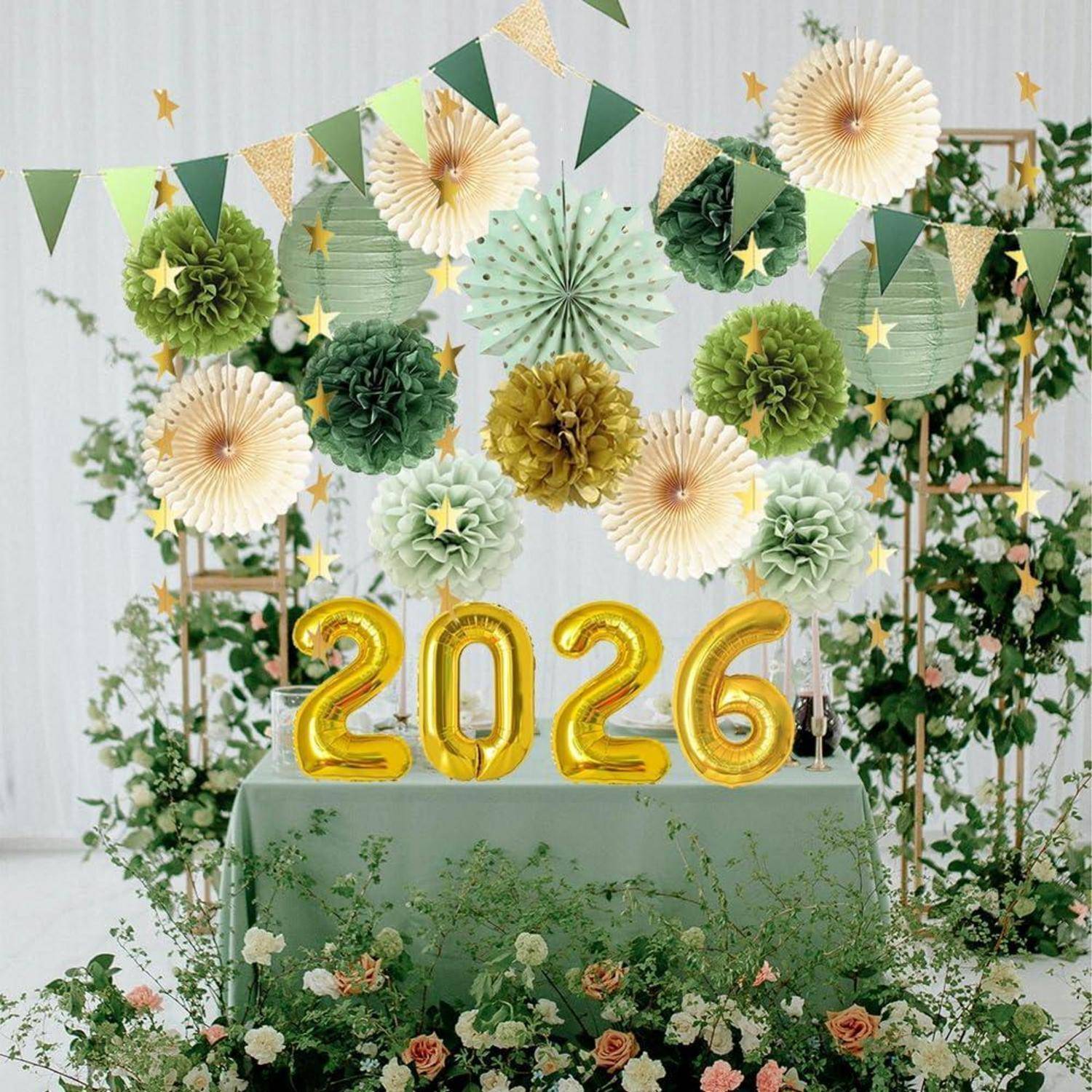 Festliche Partydekorationen 2026 mit goldenen Ballonziffern, grünen und cremefarbenen Papierdekorationen sowie blumigem Grünwerk-Hintergrund über einem dekorierten Tisch.
