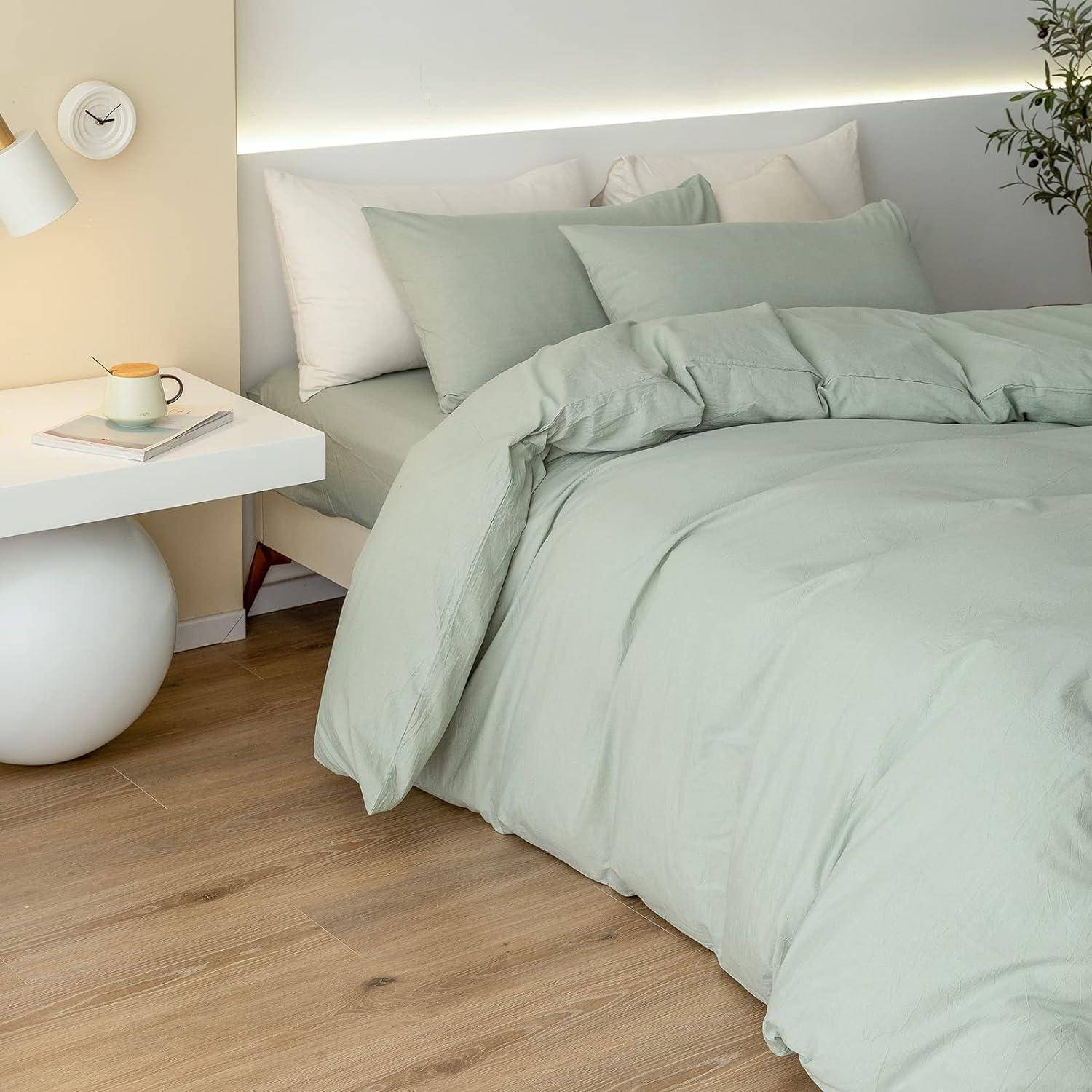 Modernes Schlafzimmer mit einem ordentlich gemachtem Bett in hellgrüner Bettwäsche neben einem weißen schwebendem Nachttisch, auf dem eine Tasse und ein Buch stehen.