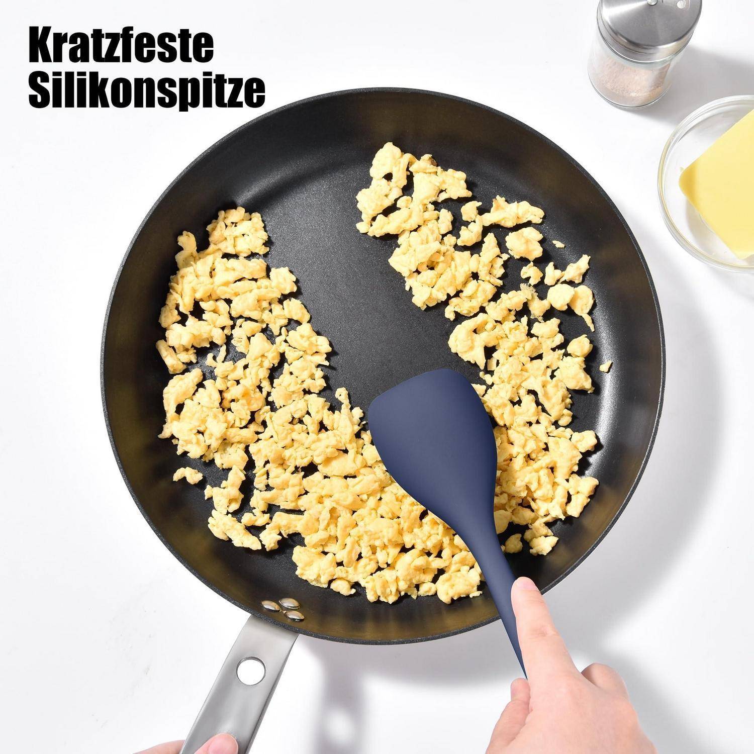 Hand mit Silikonspatel zum Umrühren von Rühreiern in einer Pfanne; deutscher Text liest sich „Kratzfeste Silikonspitze