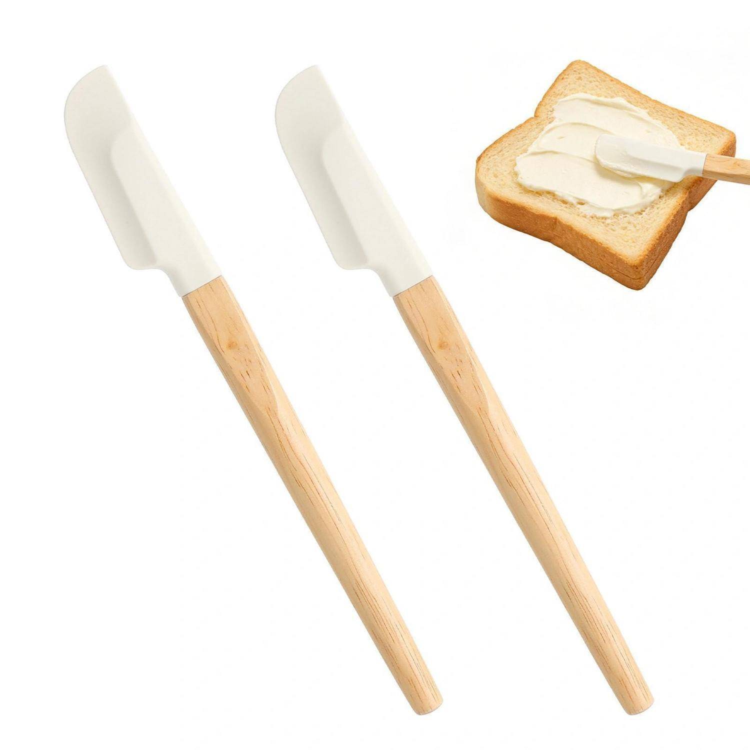 Zwei Silikonspachtel mit Holzgriffen, abgebildet neben einer Brotscheibe, die mit Butter oder Creme bestrichen wird.