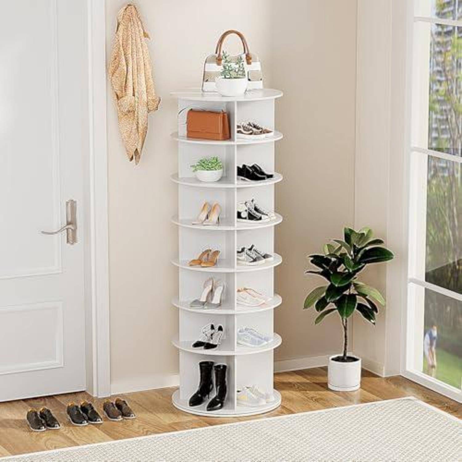 Weiß drehendes Schuhregal in einem hellen Eingangsbereich, das mehrere Paar Schuhe hält, mit einer Tasche oben drauf, neben einer Topfpflanze und einer Tür.