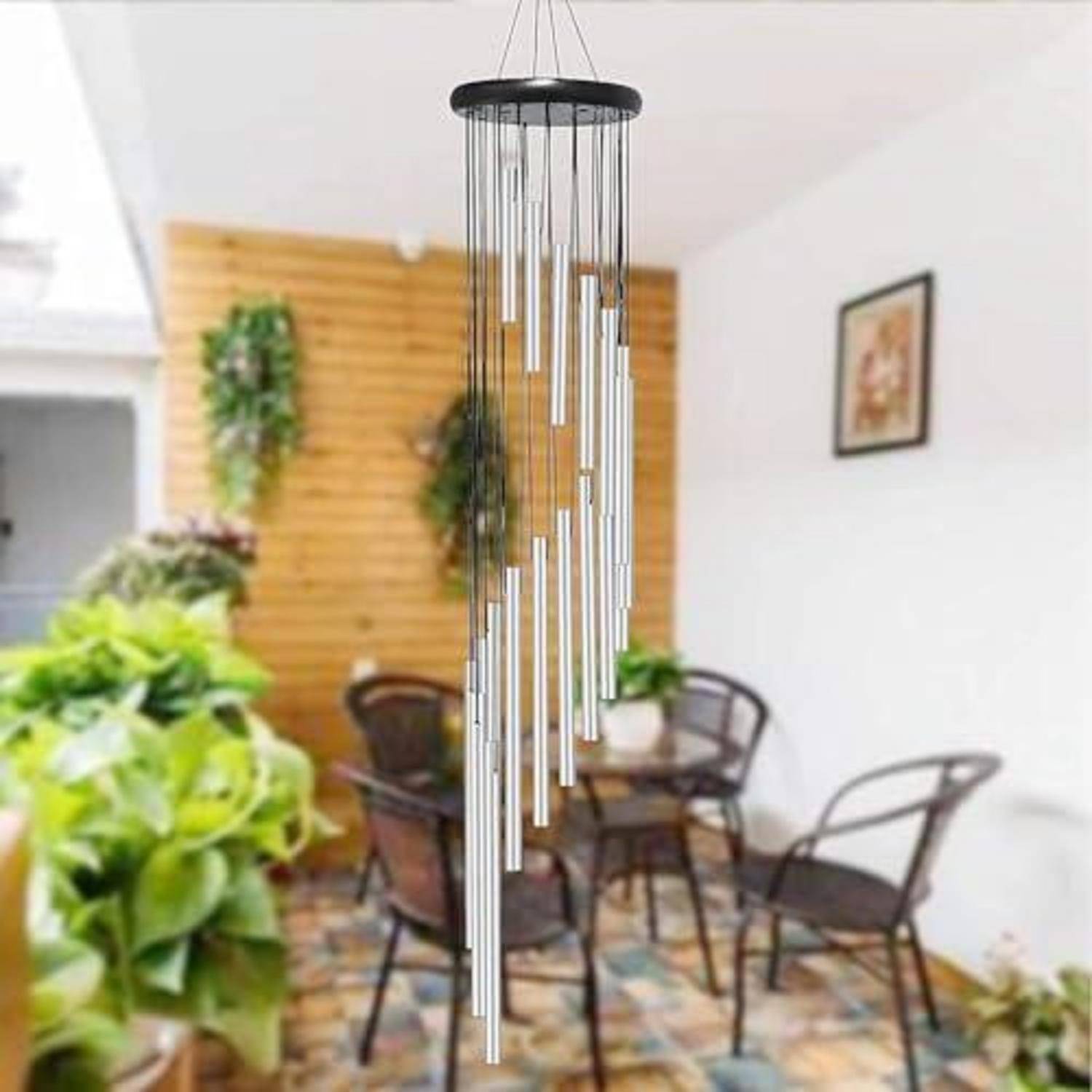 Ein hängender silberner Windspiel mit langen Röhren in einem Terrassensitzbereich, umgeben von Pflanzen und Stühlen.