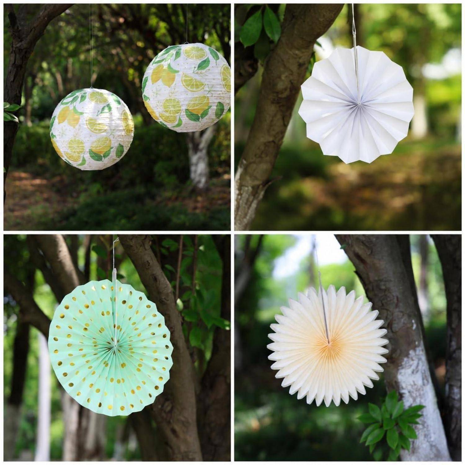 Vier dekorative hängende Papiergirlanden/Rosetten in einem Baum: zwei gemusterte Kugeln, ein weißer Fächer, ein mintfarbener Fächer mit Punkten und ein weiß-goldener Fächer.