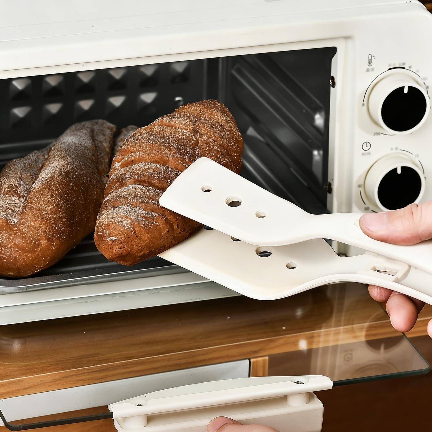 Hand benutzt weiße Ofenhandschuhe und Zangen, um einen Laib Brot aus einem Toasterofen zu entnehmen.