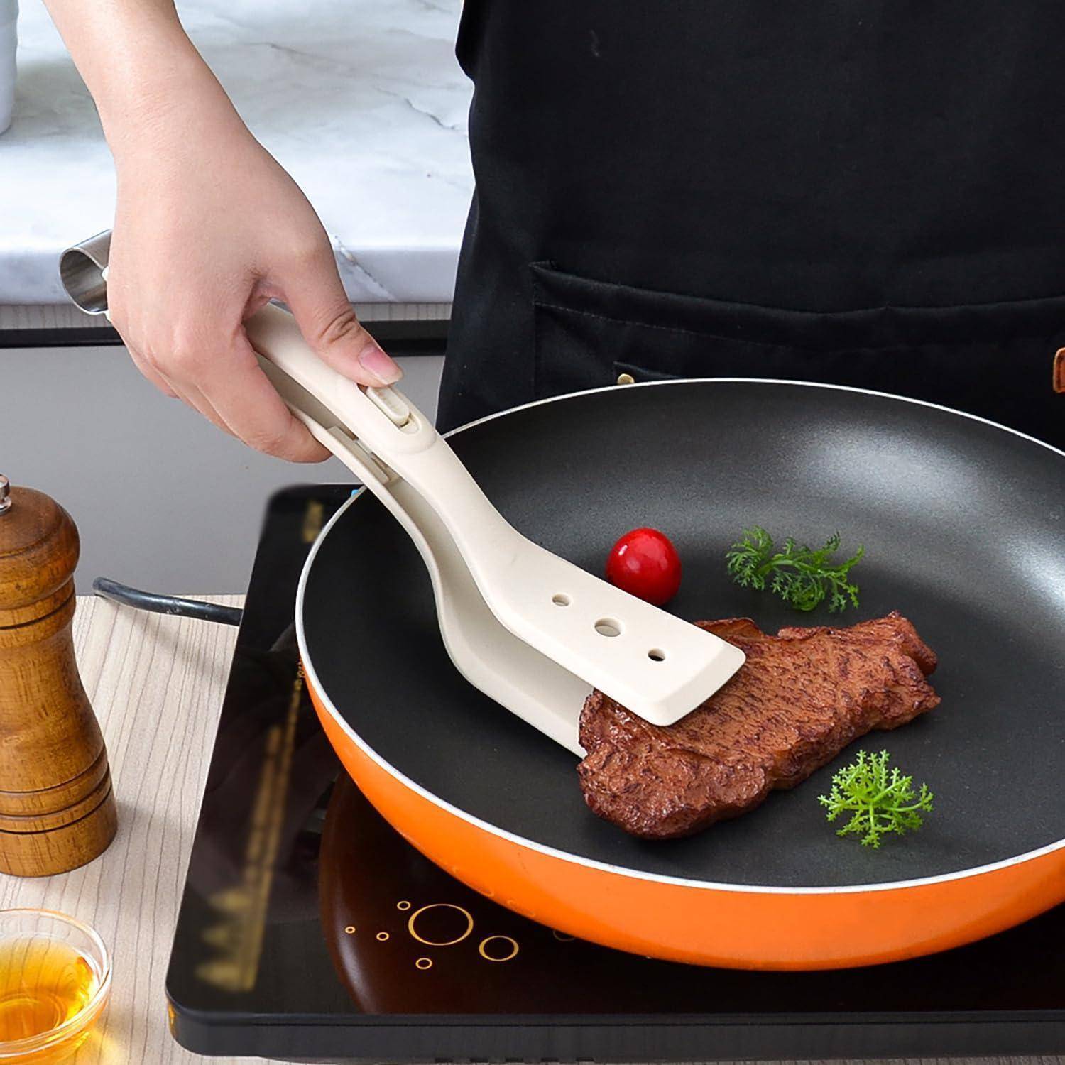 Eine Hand, die weiße Zangen hält, hebt ein angebratenes Steak aus einer orangefarbenen Pfanne auf einem Kochfeld, wobei Petersilie und eine Kirschtomaten in der Nähe sind.