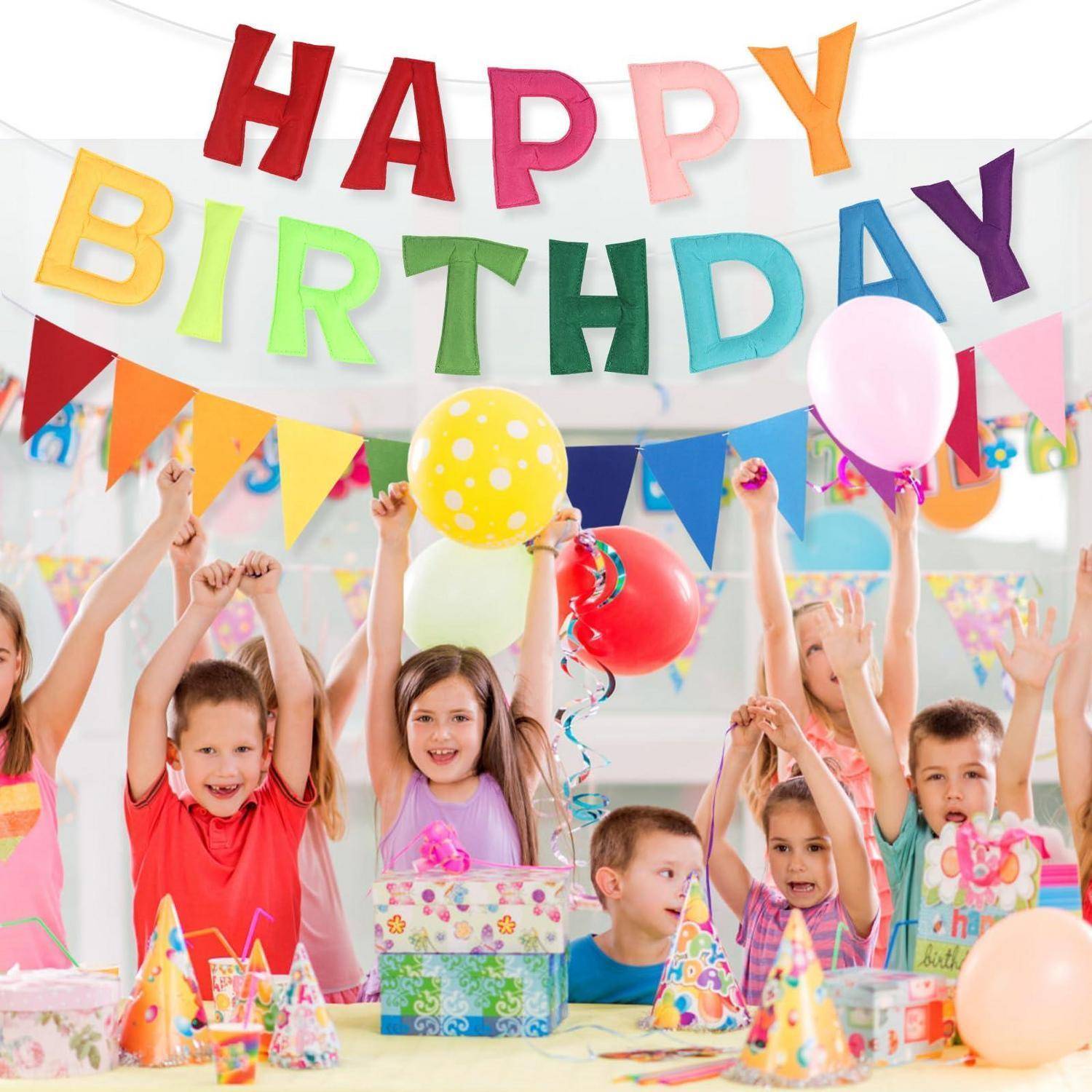 Kinder, die eine Geburtstagsfeier mit einem „ALLES GUTE ZUM GEBURTSTAG"-Banner, Ballons und Partyhüten um einen Geschenktisch herum feiern.