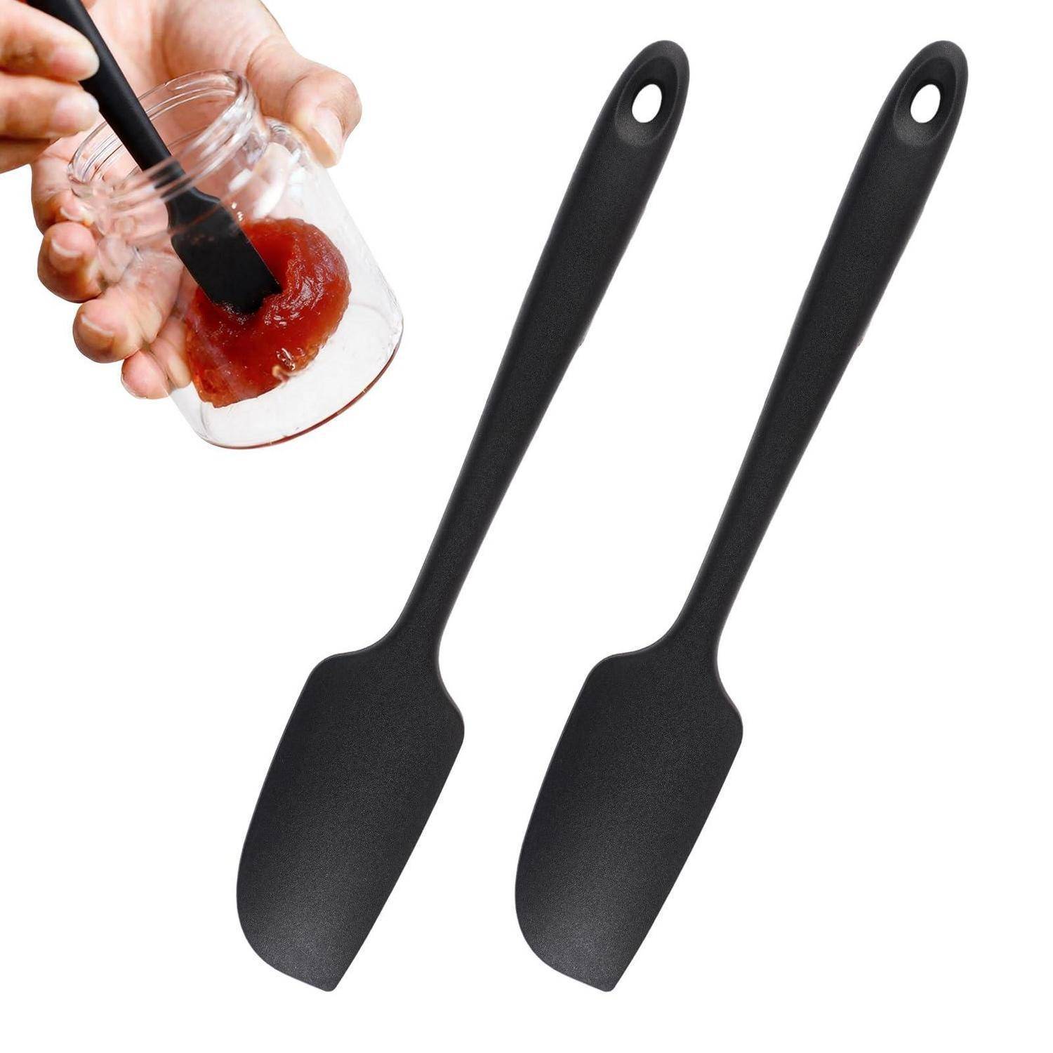 Zwei schwarze Silikonspachteln mit Aufhängelöchern, dazu eine kleine Detailansicht, die zeigt, wie eine von ihnen Sauce in einem Glas umrührt.