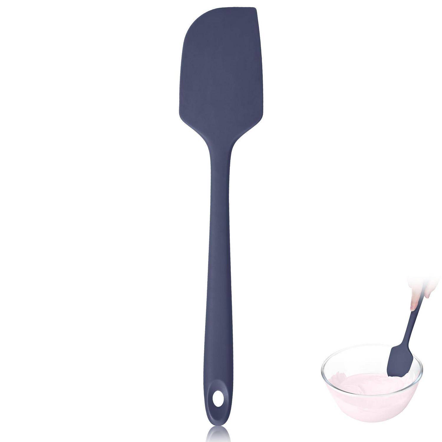 Dunkelblau silikon spatel mit aufhängeloch, gezeigt mit einem kleinen ausschnitt beim mischen von rosa teig in einer glassschüssel.
