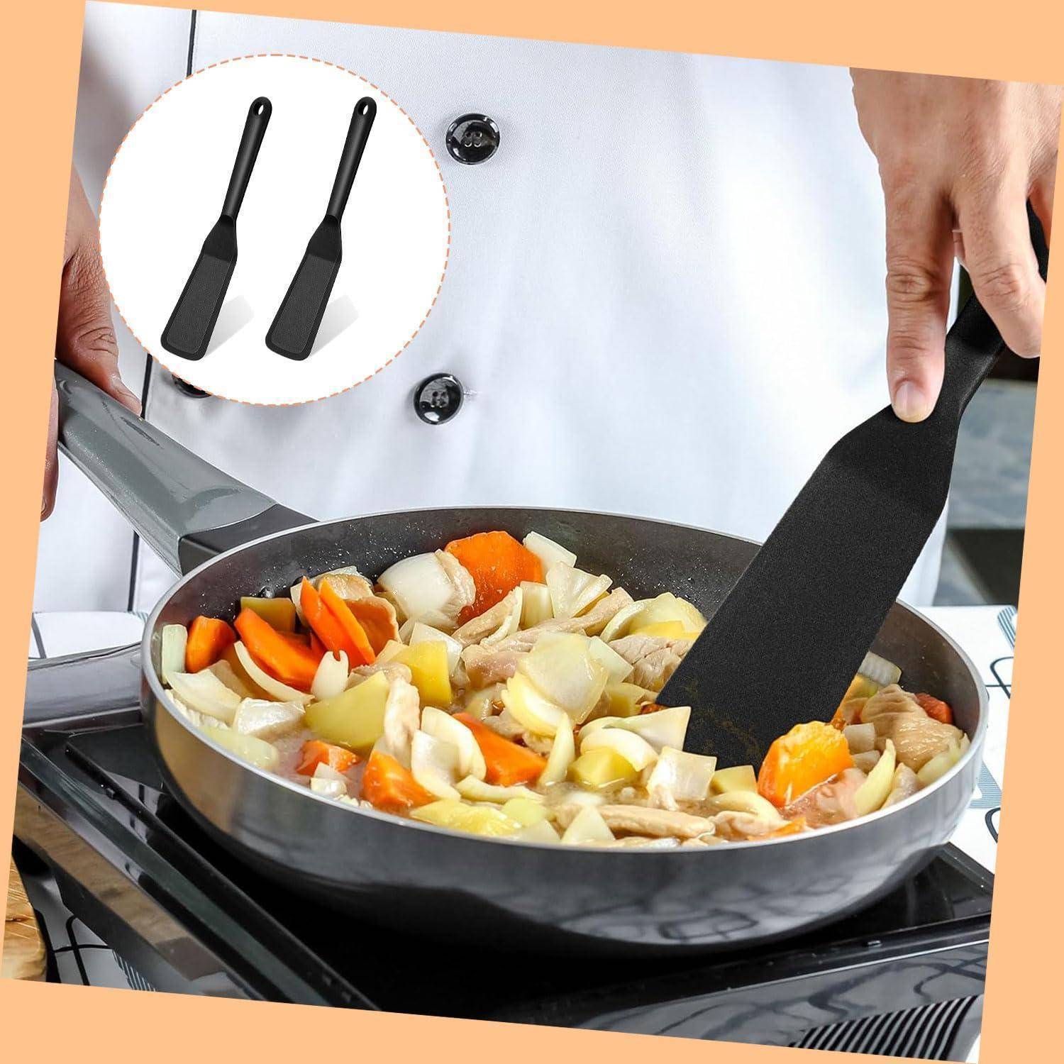 Chef rührt Gemüse-Pfanne in einer Pfanne auf einem Herd um, wobei zwei schwarze Spatel in einer Einfügung gezeigt werden, die die Kochutensilien hervorhebt.