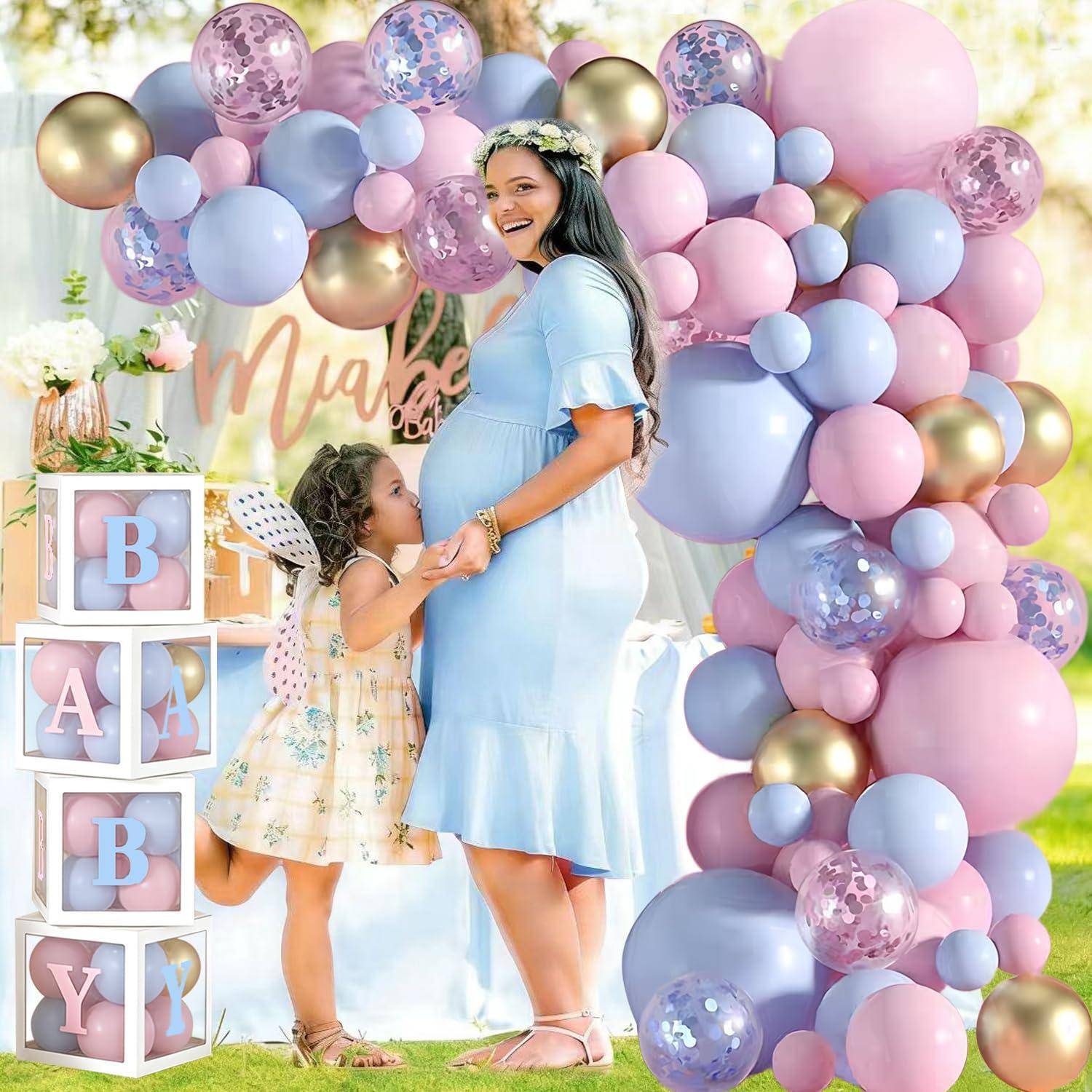Schwangere Frau in einem hellblauen Kleid mit einem jungen Mädchen an einem Pastellballon-Babyparty-Bogen, mit "Baby""-Blöcken und einem ""Maybe""-Schild.
