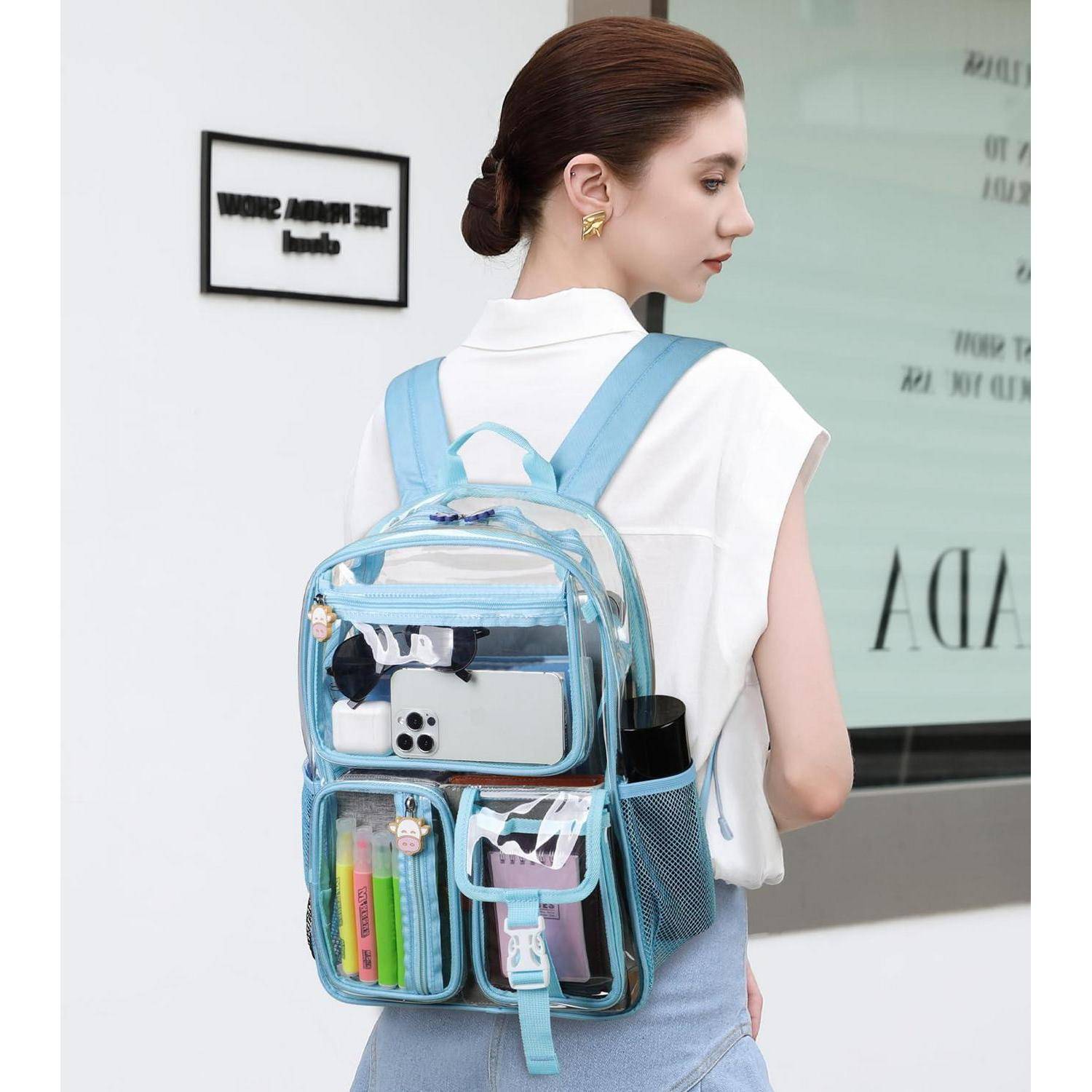 Frau, die einen transparenten blauen Rucksack mit einem Telefon, einer Wasserflasche und Schreibwaren trägt, dargestellt in der Seitenansicht im Innenbereich.