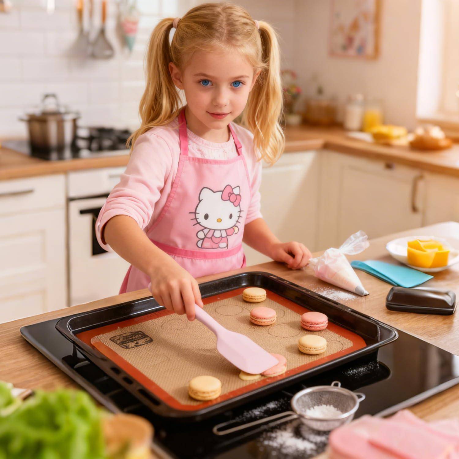 Junges Mädchen in einer rosa Hello-Kitty-Schürze backt Makronen und legt eines auf ein Tablett in einer hellen Küche.