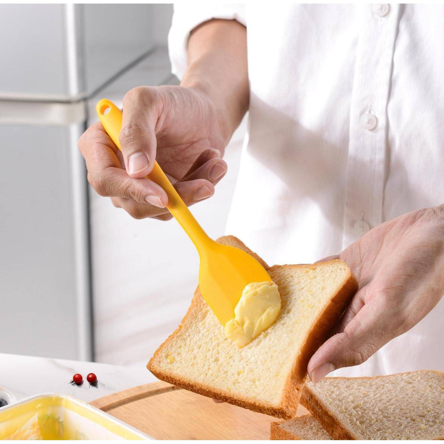 Eine Person verbreitet Butter auf einer Scheibe Weißbrot mit einem gelben Spachtel in einer Küche.