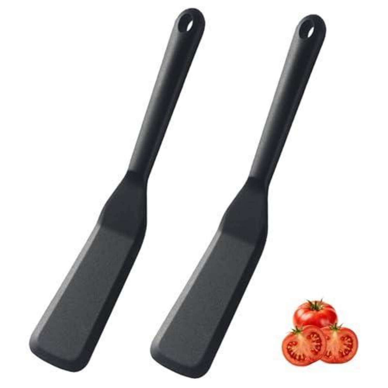 Zwei schwarze Spachteln mit Schlitzen und Aufhängelöchern, gezeigt mit geschnittenen Tomaten, um die Küchenverwendung zu suggerieren.