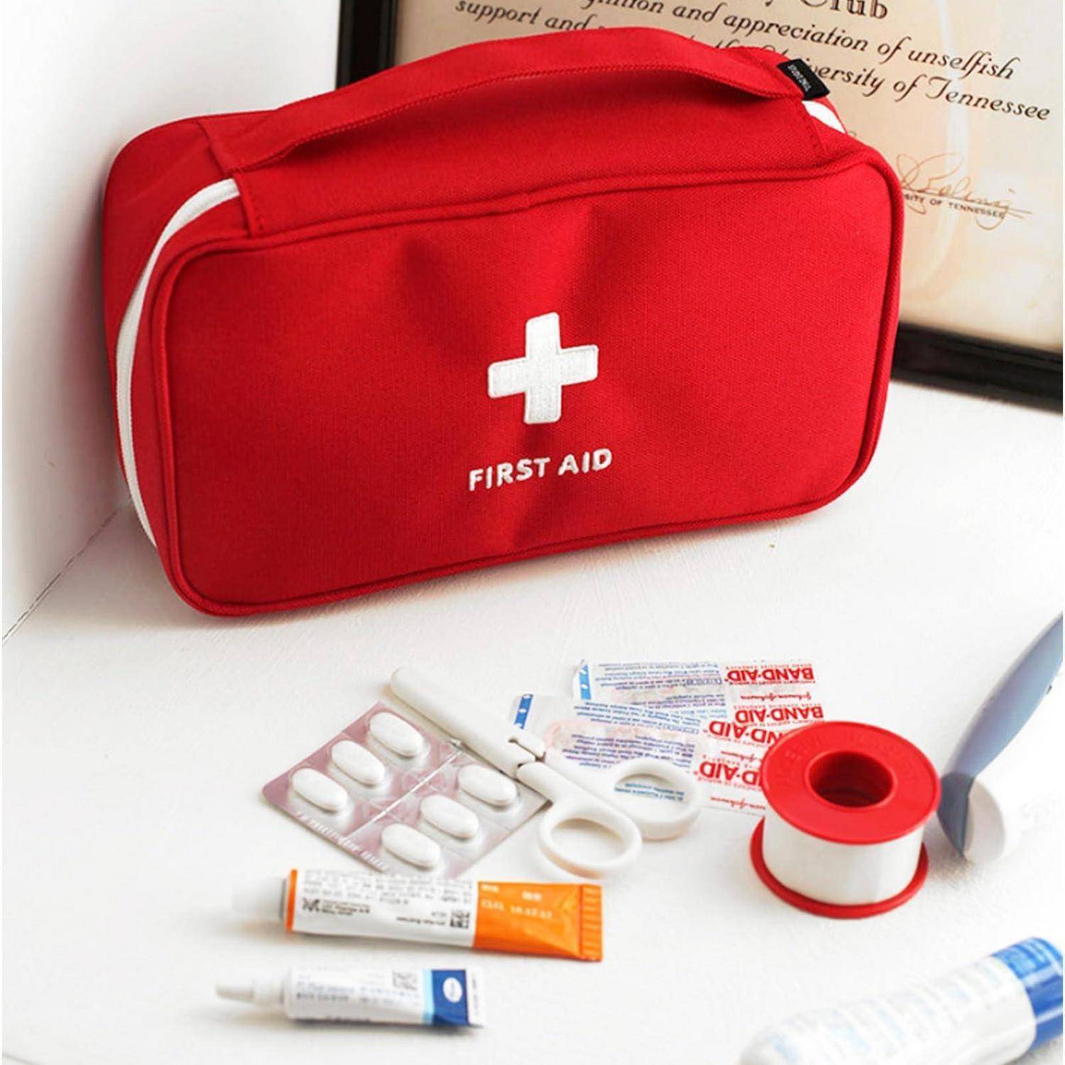 Rote Erste-Hilfe-Tasche mit Medizinprodukten, die darunter angeordnet sind, einschließlich Verbandsmaterial, Salben, Schere und Klebeband.