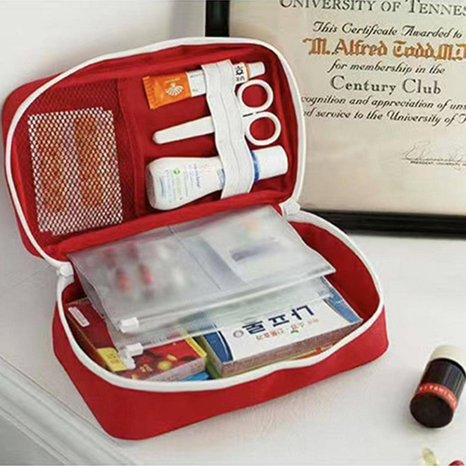 Offener roter Erste-Hilfe-Koffer mit Medizinprodukten, Salben, Schere und Verbandsmaterial auf einem Tisch, mit einem Zertifikat im Hintergrund.