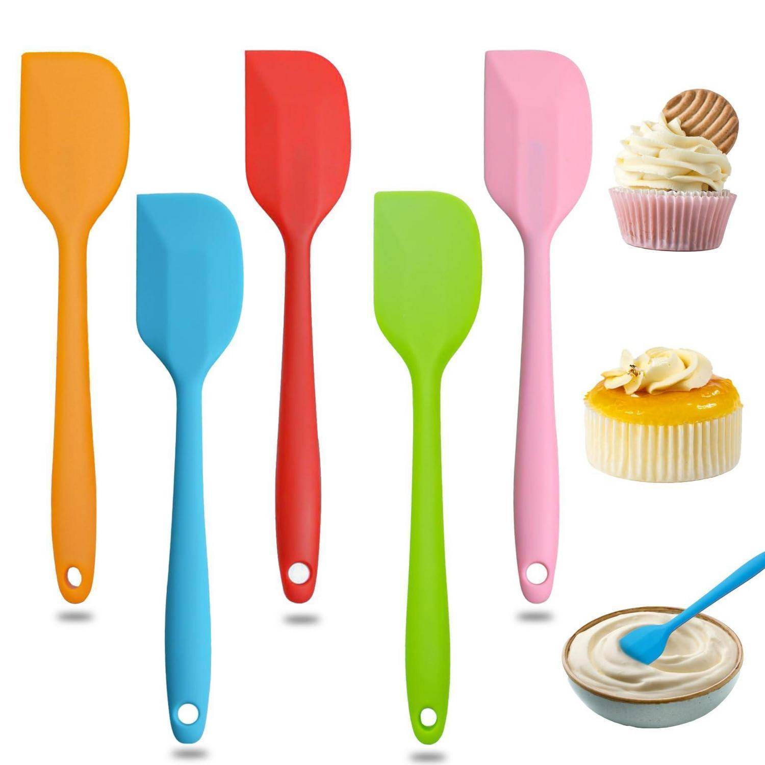 Bunte Silikonspatel in Orange, Blau, Rot, Grün und Rosa neben Cupcakes und einer Schüssel mit Zuckerguss, die Backwerkzeuge und Dekorationszutaten zeigen.