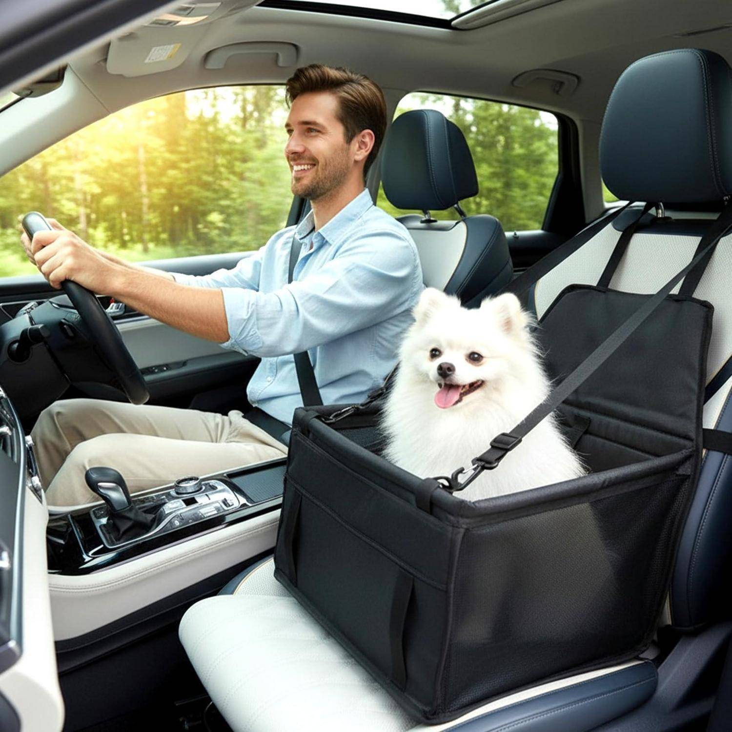 Ein lächelnder Mann fährt ein Auto, während ein kleiner weißer Hund gesichert in einem schwarzen Haustier-Boostersitz auf dem vorderen Beifahrersitz sitzt.