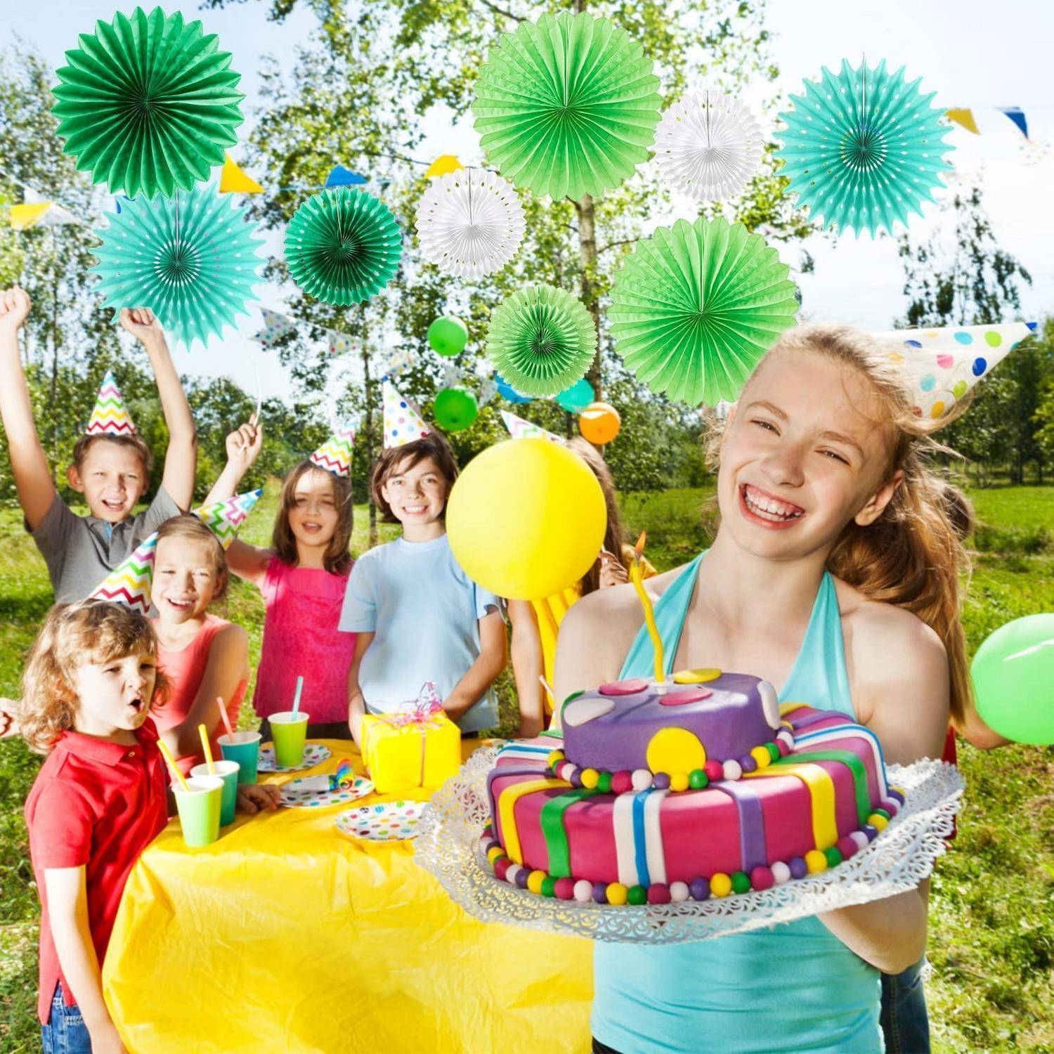 Kinder auf einer Geburtstagsfeier im Freien, mit einem lachenden Mädchen, das einen dekorierten Kuchen im Vordergrund hält, und anderen Kindern, die dahinter mit Ballons und Partyhüten feiern.