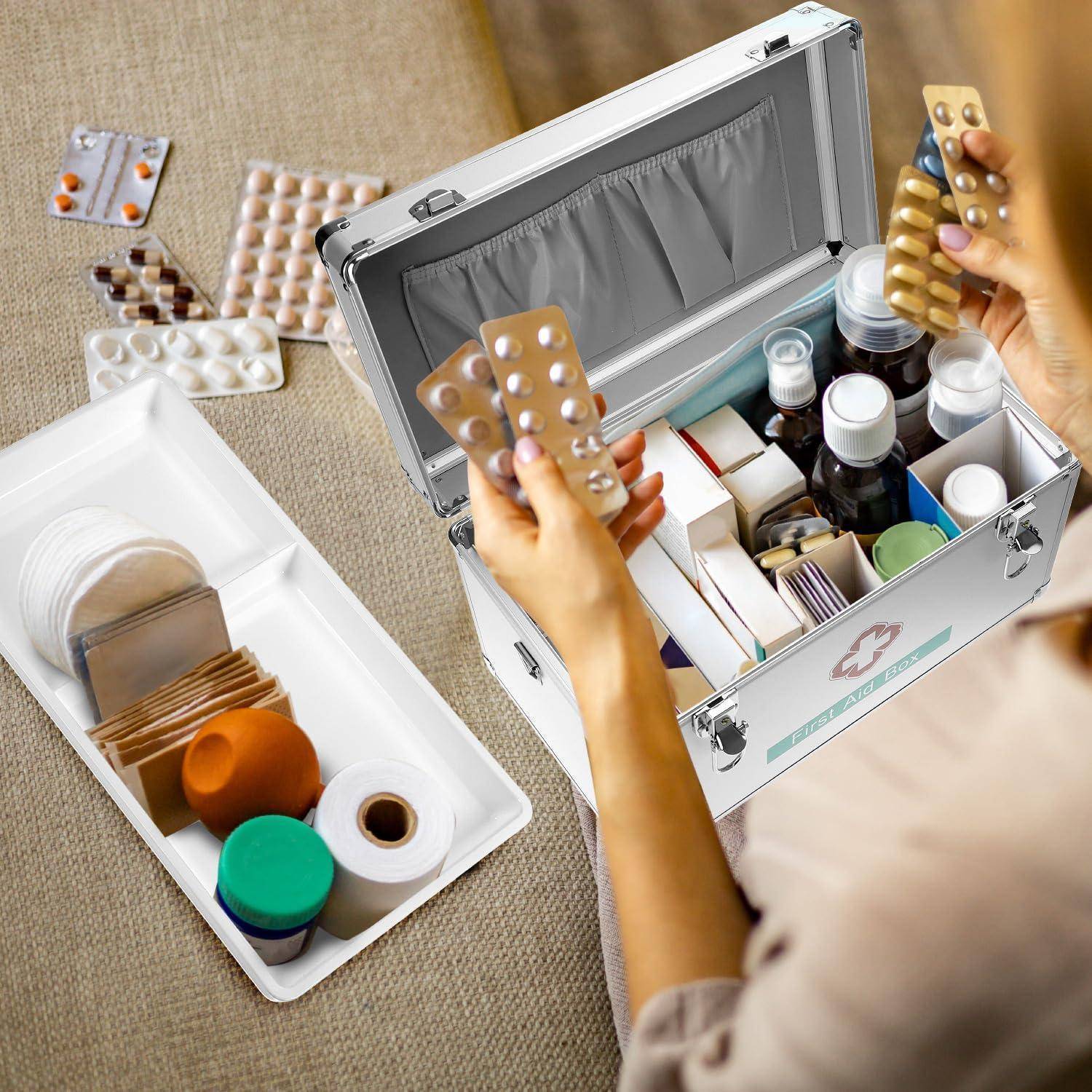 Person packt verschiedene Medikamente und Pillenblisterpackungen in einen Erste-Hilfe-Koffer neben einem Tablett mit zusätzlichen medizinischen Materialien.