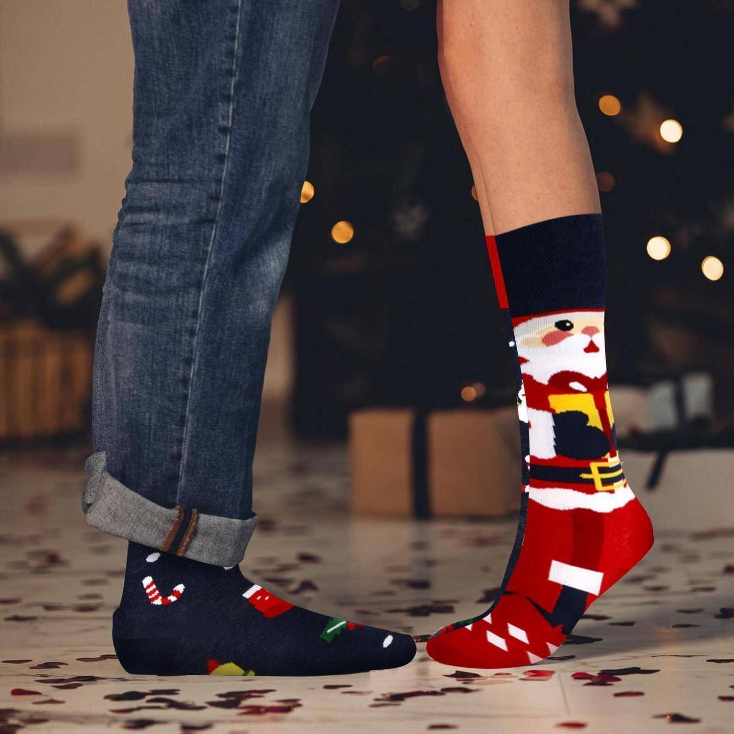 Zwei Personen, die dicht beieinander stehen und festliche ungleiche Weihnachtssocken zeigen: eine schwarze mit Zuckerstangen, eine rote mit dem Weihnachtsmann.