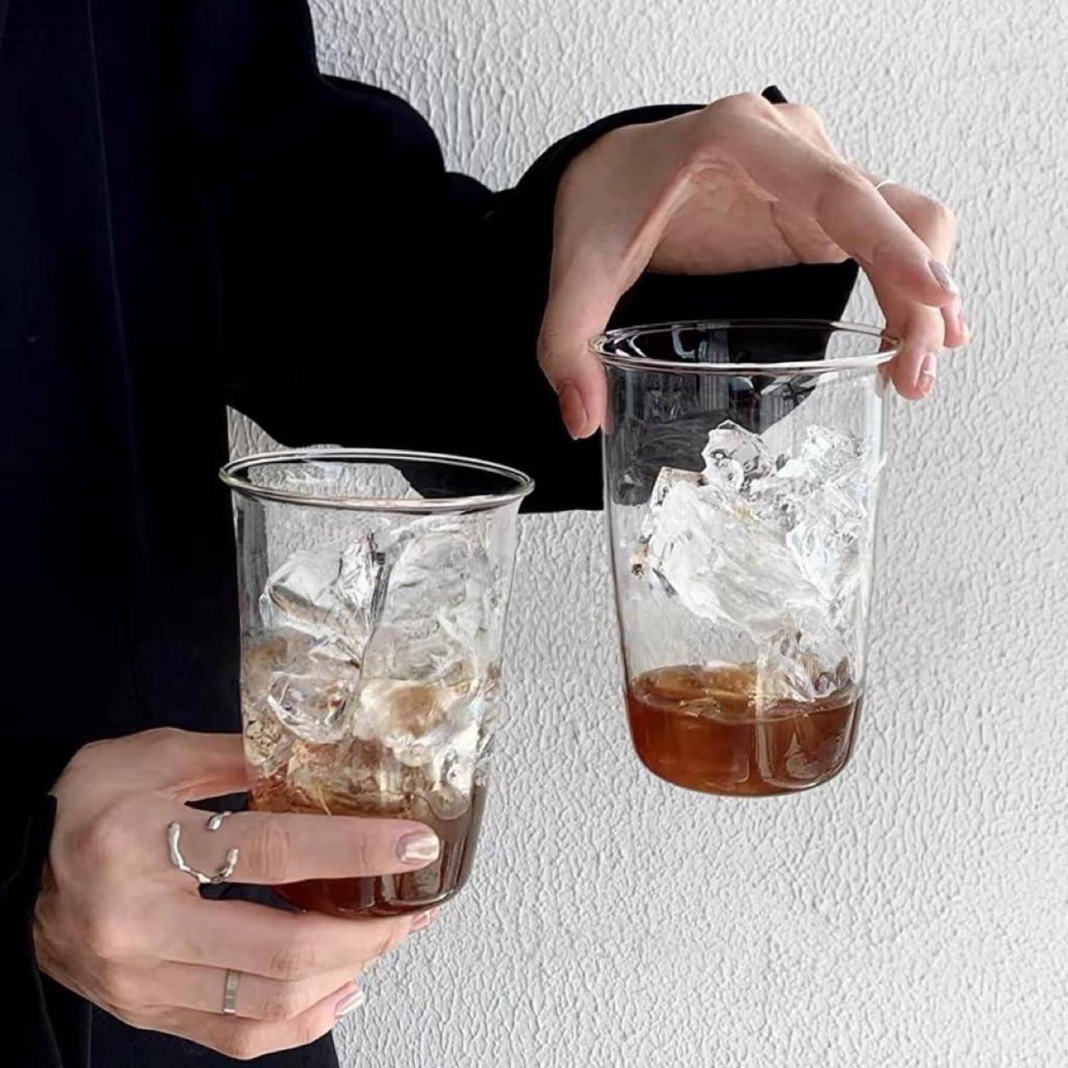 Hände halten zwei durchsichtige Kunststoffbecher mit Eis und einer kleinen Menge braunem Getränk