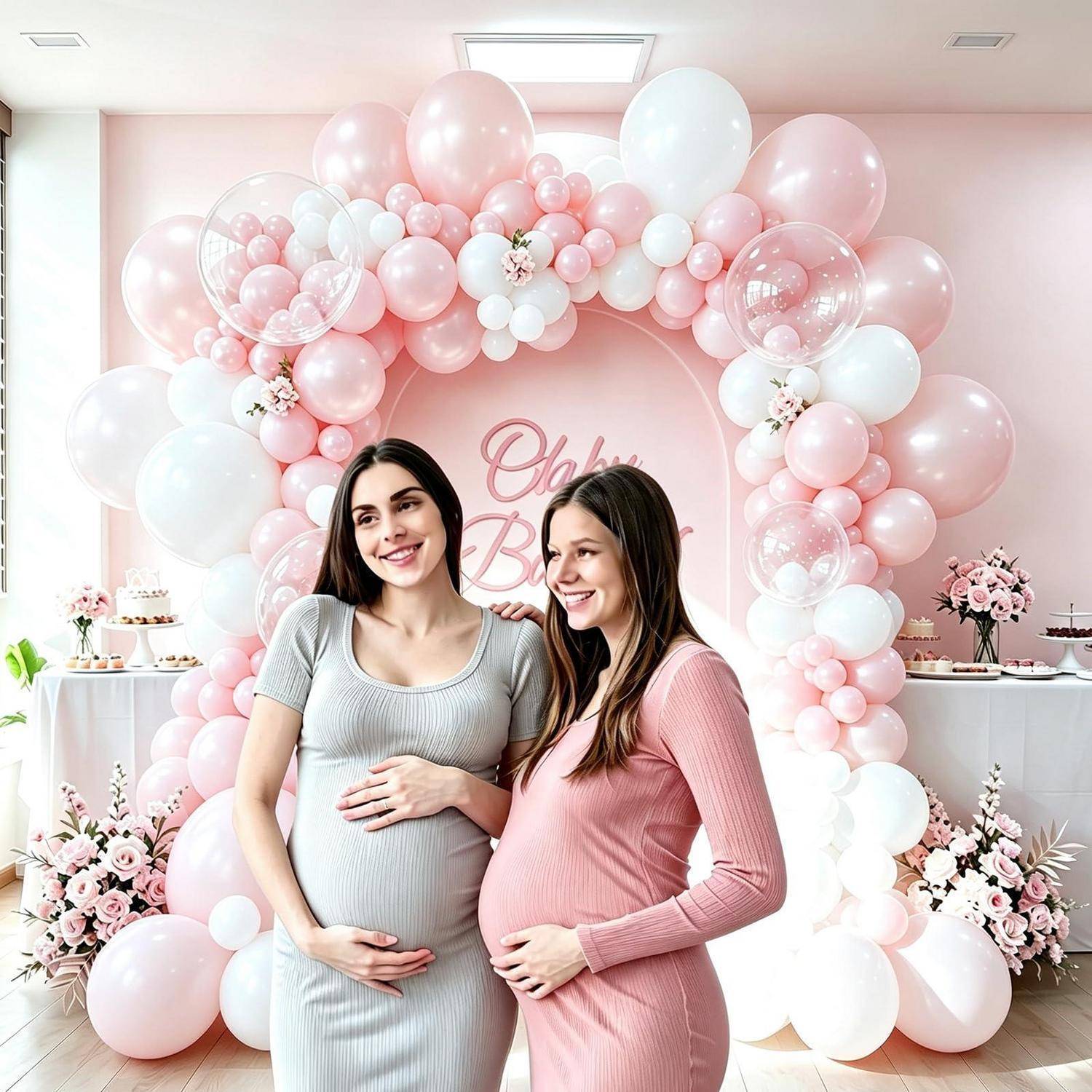 Zwei schwangere Frauen posieren bei einer rosa Baby-Shower vor einer Ballongirlande und einem „Baby"-Schild, lächeln und halten ihre Bäuche.