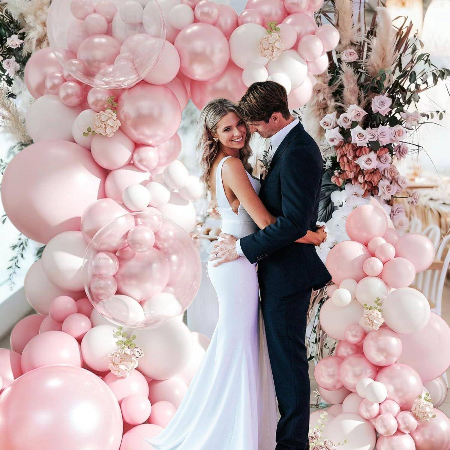 Braut und Bräutigam umarmen sich unter einem rosa Ballonbogen, wahrscheinlich bei einer Hochzeits- oder Verlobungsfeier, mit Blumendekoration um sie herum.