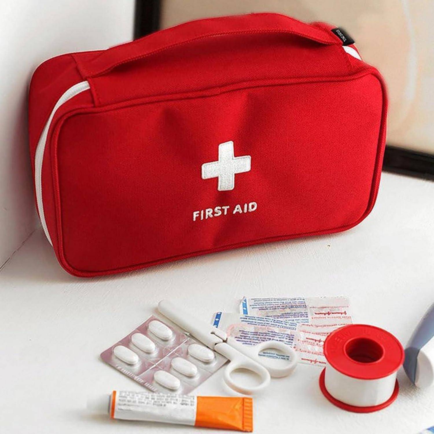 Rote Erste-Hilfe-Tasche mit weißem Kreuz und der Aufschrift „ERSTE HILFE", umgeben von verschiedenen medizinischen Utensilien wie Tabletten, Verbandsmaterialien, Klebeband und einer Salbentuber.