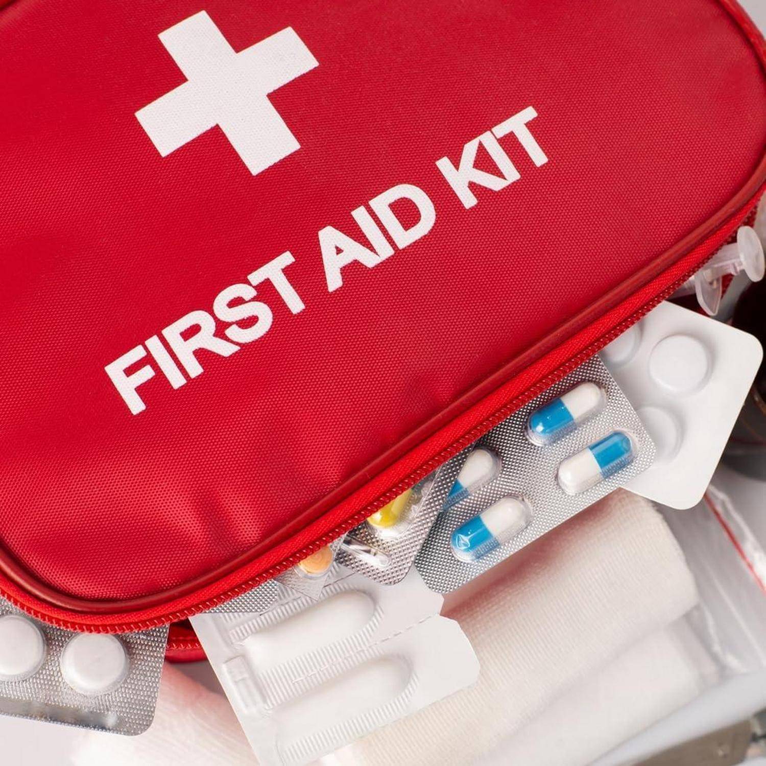 Rote Erste-Hilfe-Tasche mit weißem Kreuz und der Aufschrift "FIRST AID KIT"", teilweise geöffnet, um verschiedene Medikamente, Verbandsmaterialien und medizinische Utensilien zu zeigen.