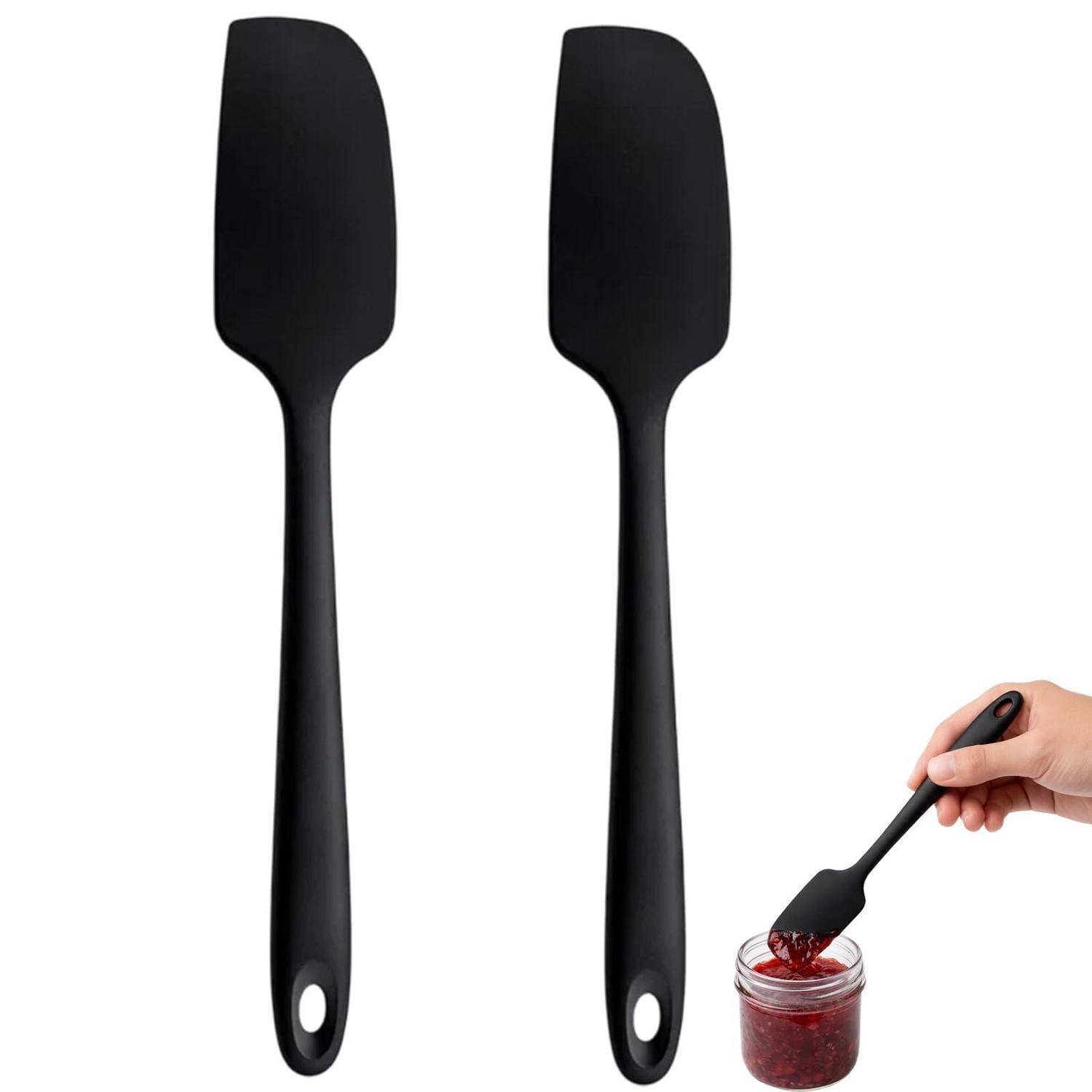 Zwei schwarze Silikon-Spatel aufrecht dargestellt, wobei einer zum Umrühren von roter Marmelade in einem Glasglas verwendet wird.